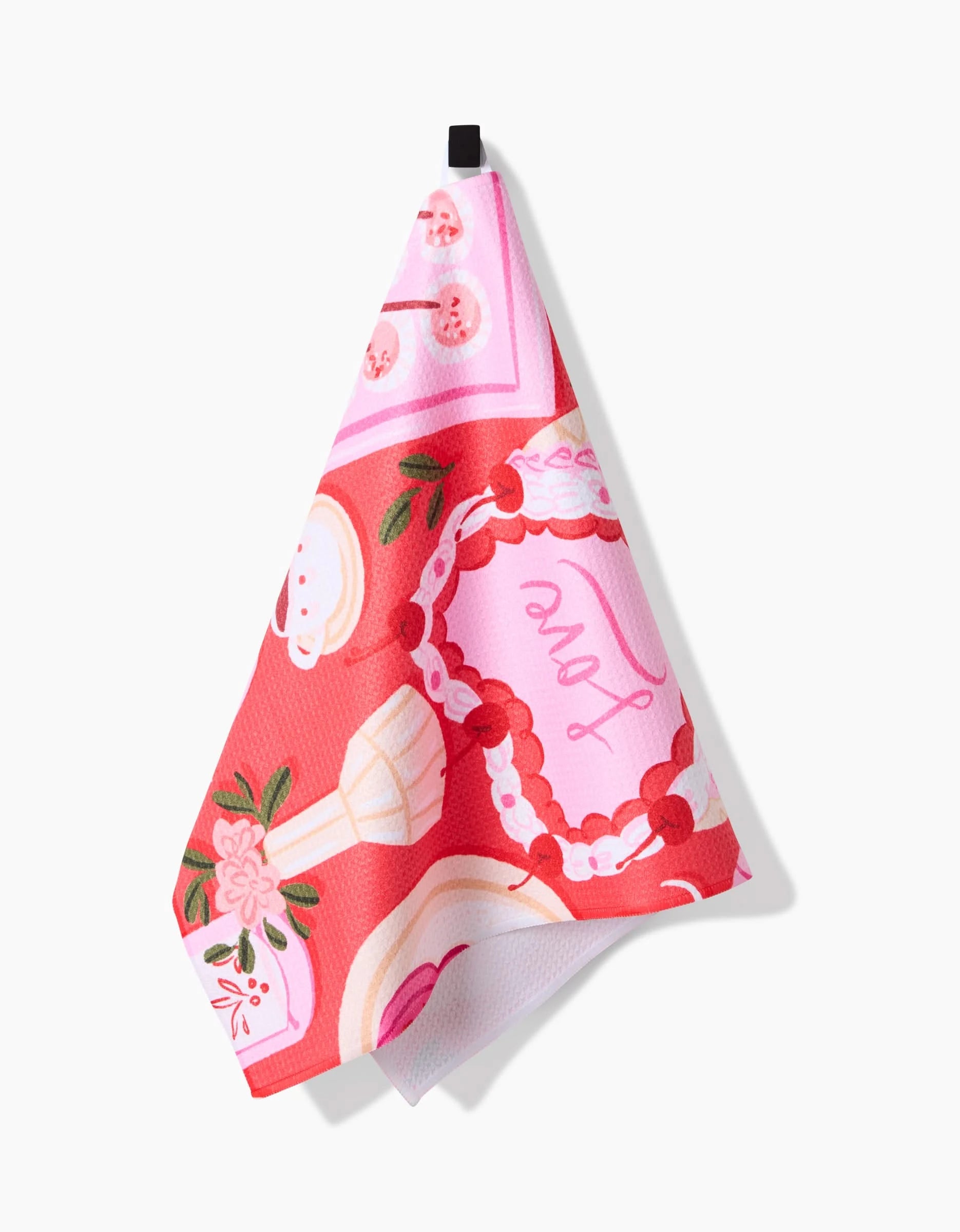 The Food of Love tea towel by Janna Sue Design features illustrated cakes, cherries, flowers, and Love in script on recycled pink and red fabric. It hangs from a black loop against a white background.