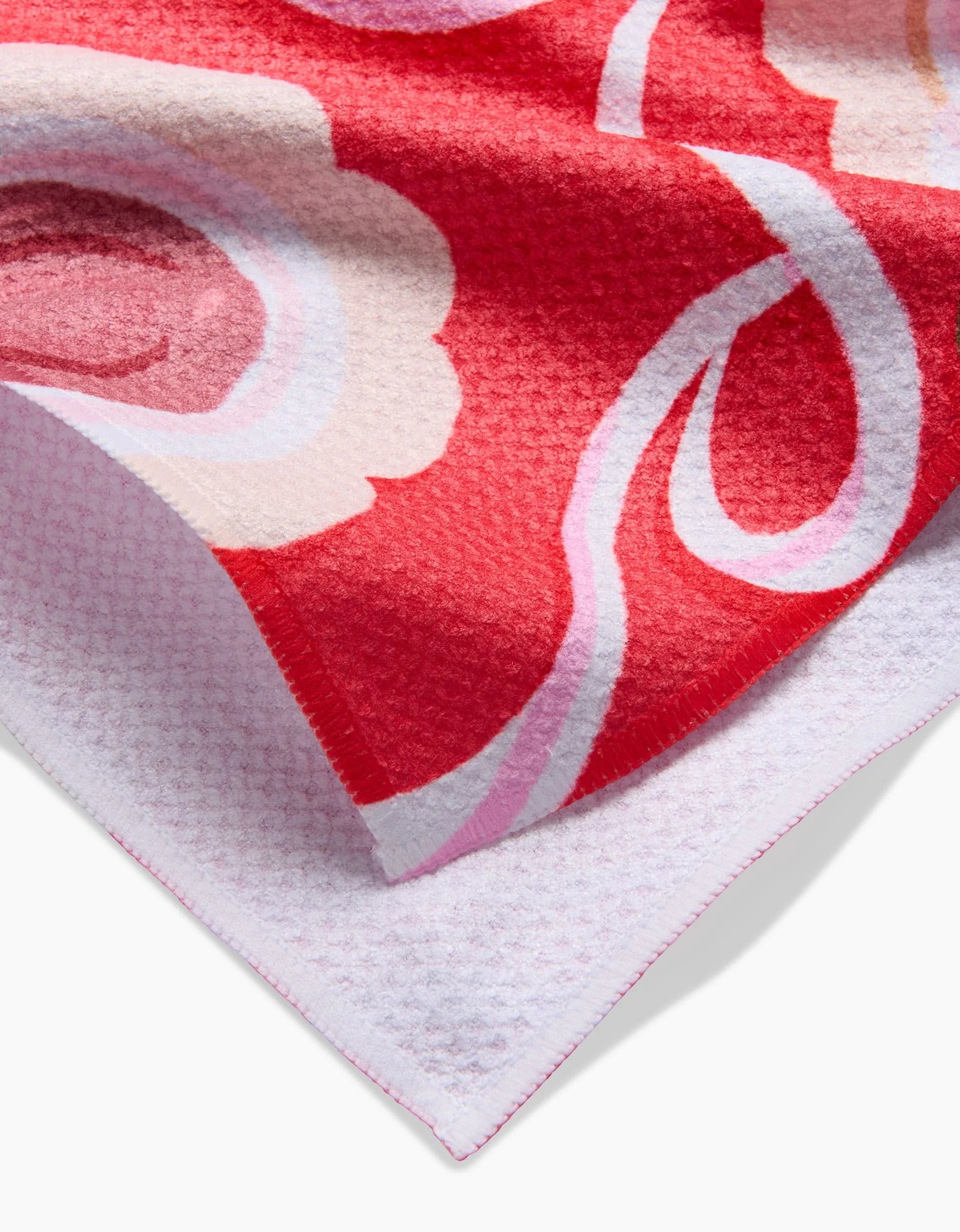 A close-up of Food of Love by Janna Sue Design: a red and white tea towel with pink floral patterns, featuring a textured edge, contrasting white underside, and crafted from ultra-absorbent recycled materials.