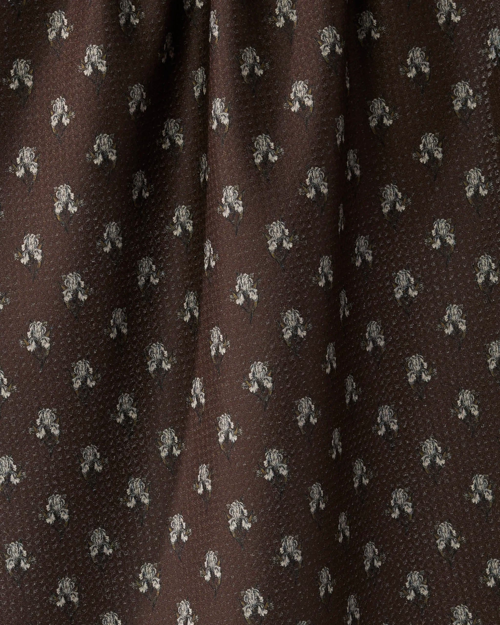 A close-up of Geometry’s Foraged recycled kitchen towel in brown, showing its subtle woven texture and repeating small white floral pattern, with gentle folds for added dimension.