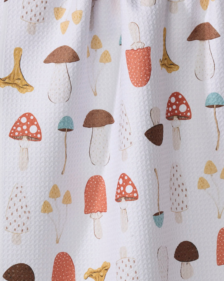 The Sara Mari "Foraging" dish towel features a white textured, absorbent fabric decorated with a colorful hand-drawn mushroom pattern in brown, red, yellow, and blue.