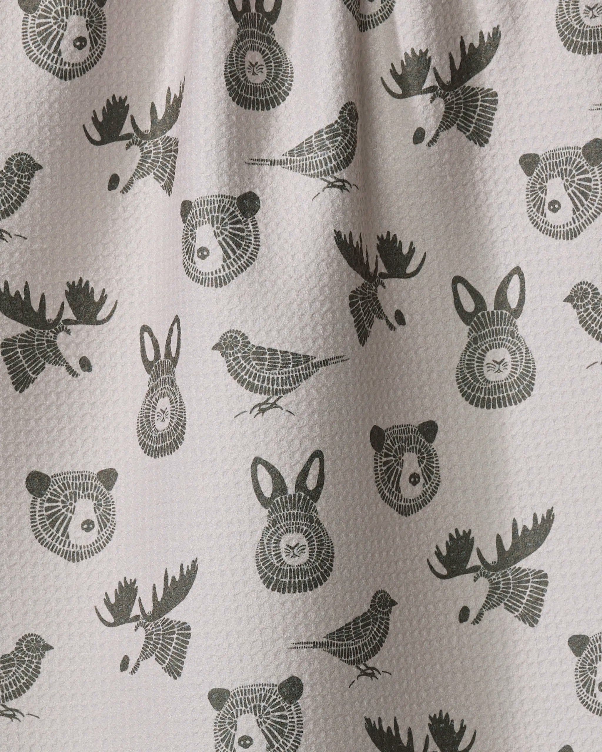 The Forest Animals kitchen towel by Rosa Kichline is white, textured, and absorbent, featuring a repeating pattern of black bears, rabbits, moose, and birds evenly spaced across the surface.