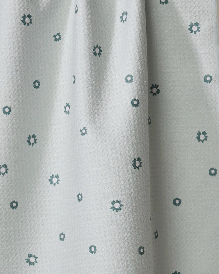 The Forest Daisy by Coit Creative is a light gray towel with small dark green and white flower patterns. Ultra-absorbent and made from recycled materials, it hangs in gentle folds—ideal as a kitchen or tea towel.