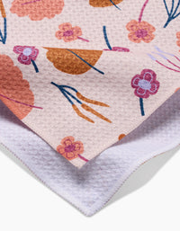 A close-up of the Claire Iglesias Forest Leaves tea towel, featuring a soft textured pink, orange, and purple floral pattern on one side and plain white Geoweave fabric on the other, neatly folded to highlight both sides.