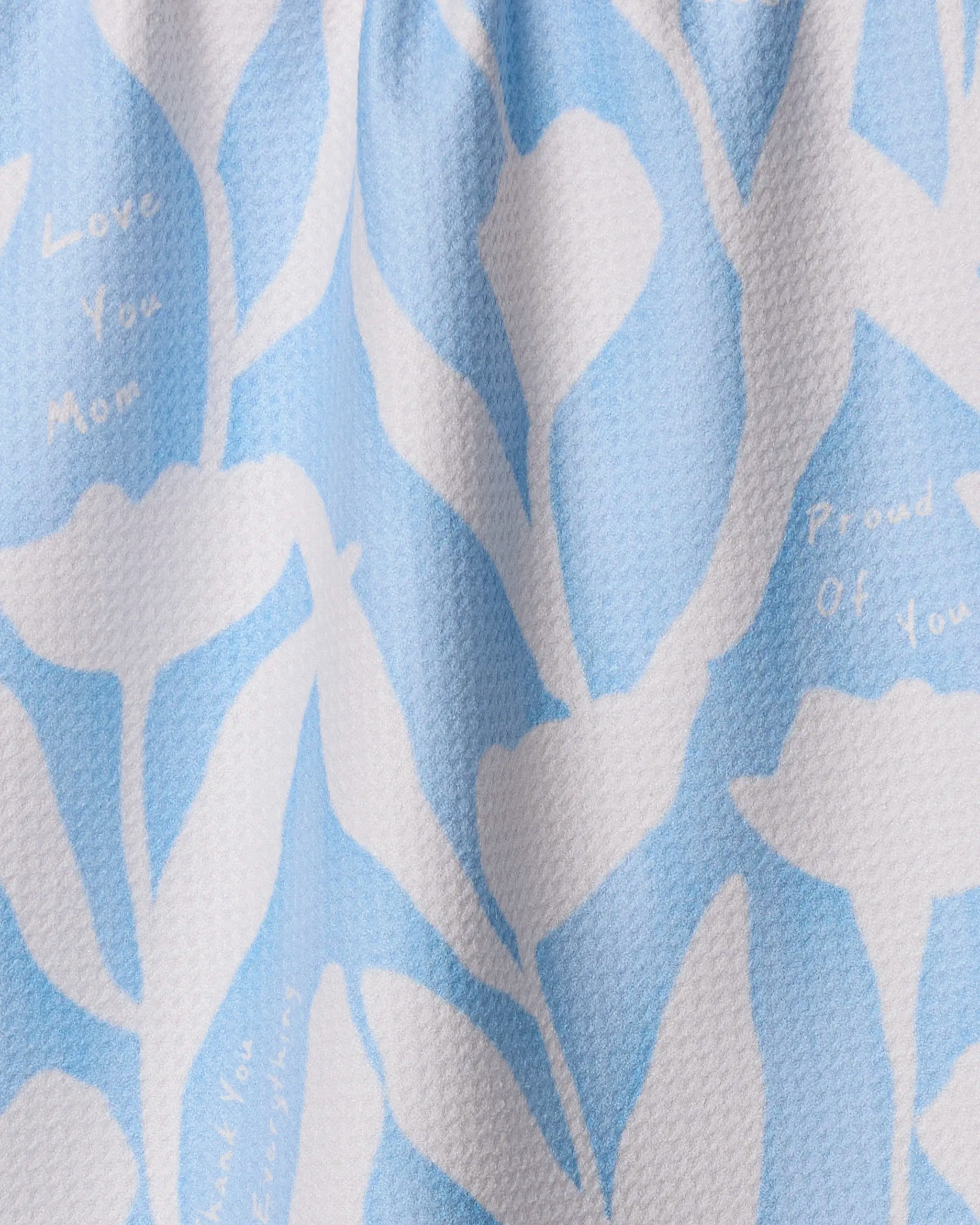 A close-up of Geometry’s Forever Grateful kitchen towel, made from recycled materials, with light blue and white abstract leaf patterns and faint words: Love You Mom, Thank You, Proud Of You, and Everlasting.