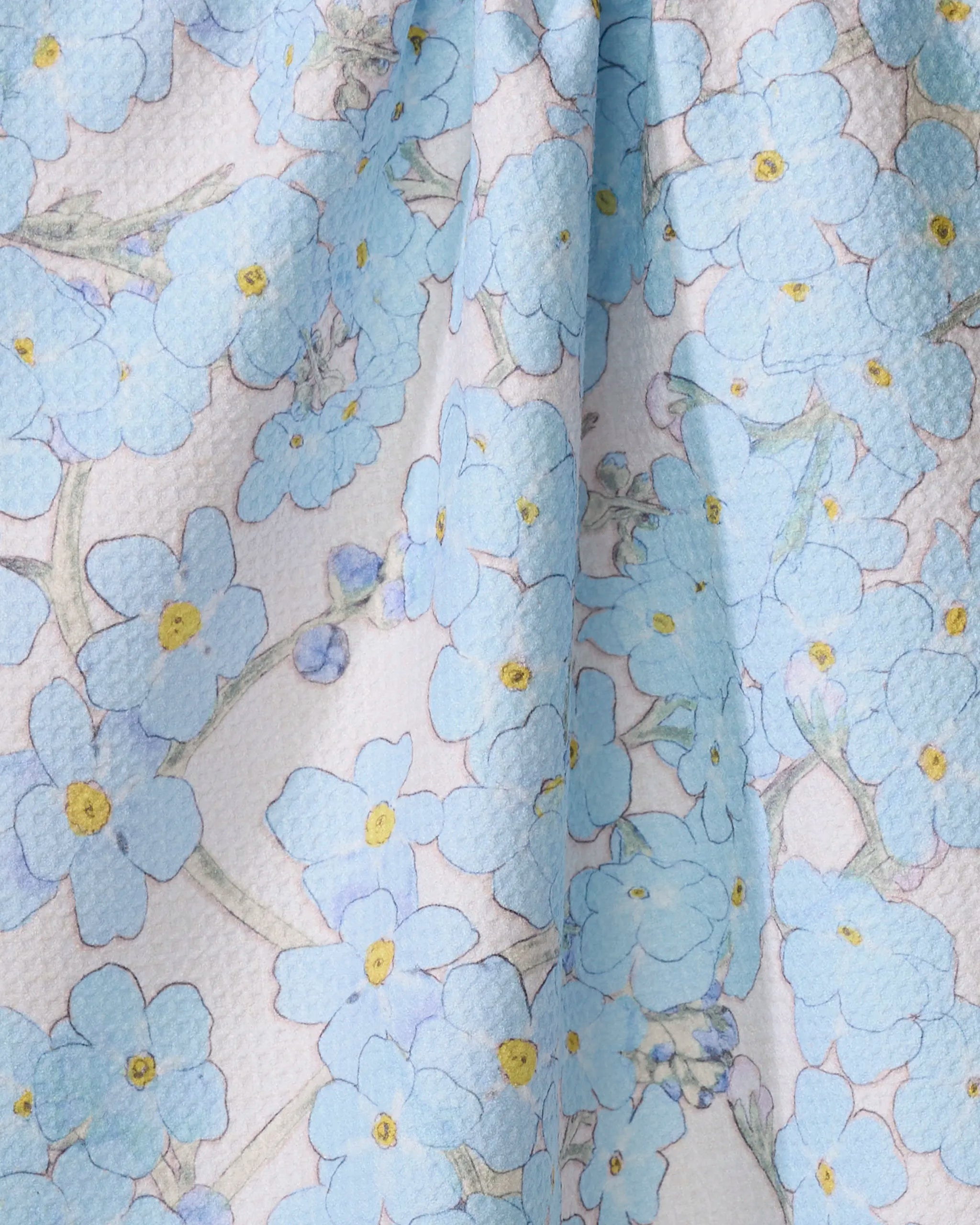 Close-up of the Pascale Dilger "Forget Me Not Floral" kitchen towel, made from recycled materials and featuring delicate light blue forget-me-nots with yellow centers and green stems on a white background.