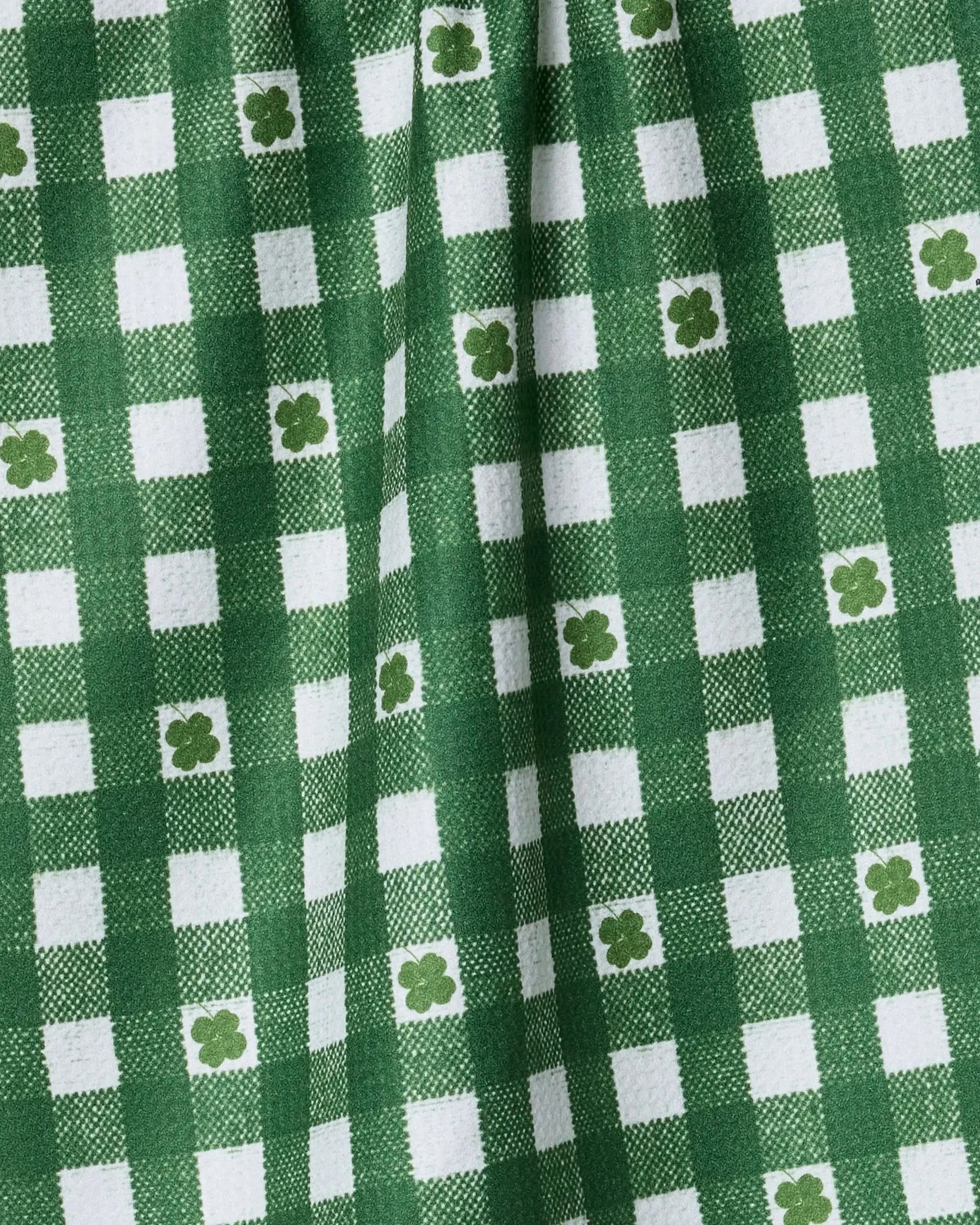 Close-up of Geometry's Fortunate Gingham tea towel—green and white checks with green four-leaf clovers in some squares. Made from recycled materials, the fabric is softly gathered to show its texture.