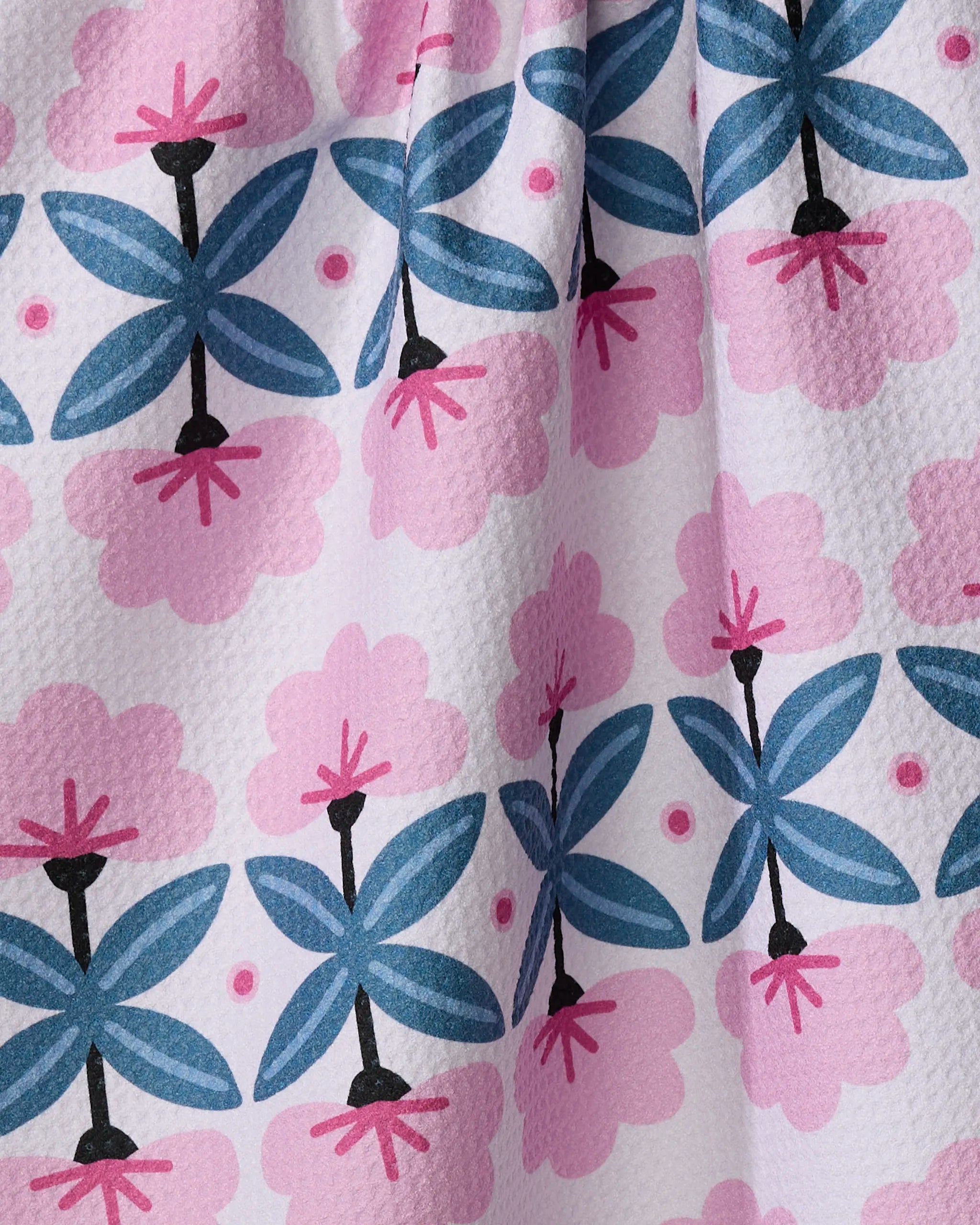 The "Fragrant Flowers" tea towel by Anette Heiberg features blue and black geometric flowers, pink floral shapes, small pink dots, and stylized petals on white—a charming, ultra-absorbent design.