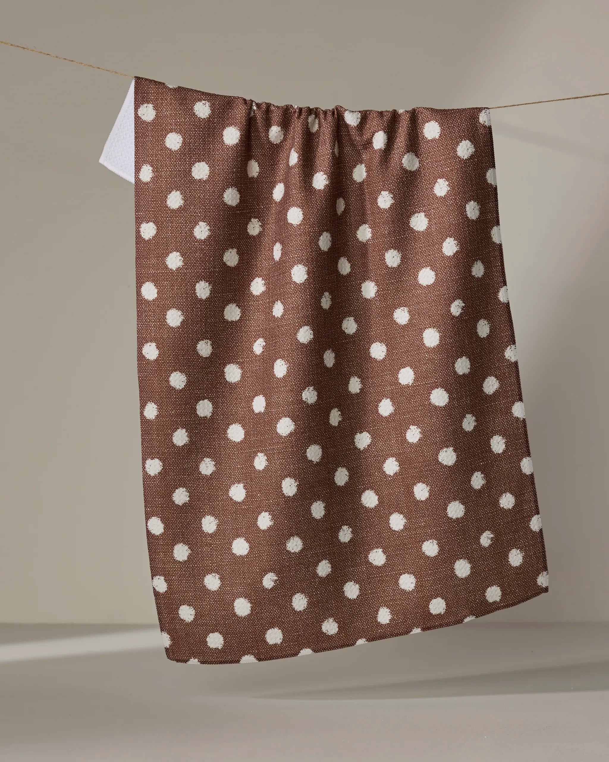 The Geometry Freckle Off White absorbent kitchen towel hangs from a clothesline against a neutral background.