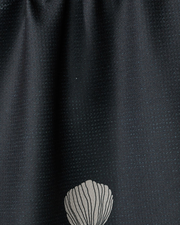 A close-up of Freja by Anna Christian shows dark recycled fabric with a subtle dotted texture and a single white seashell design near the bottom center.