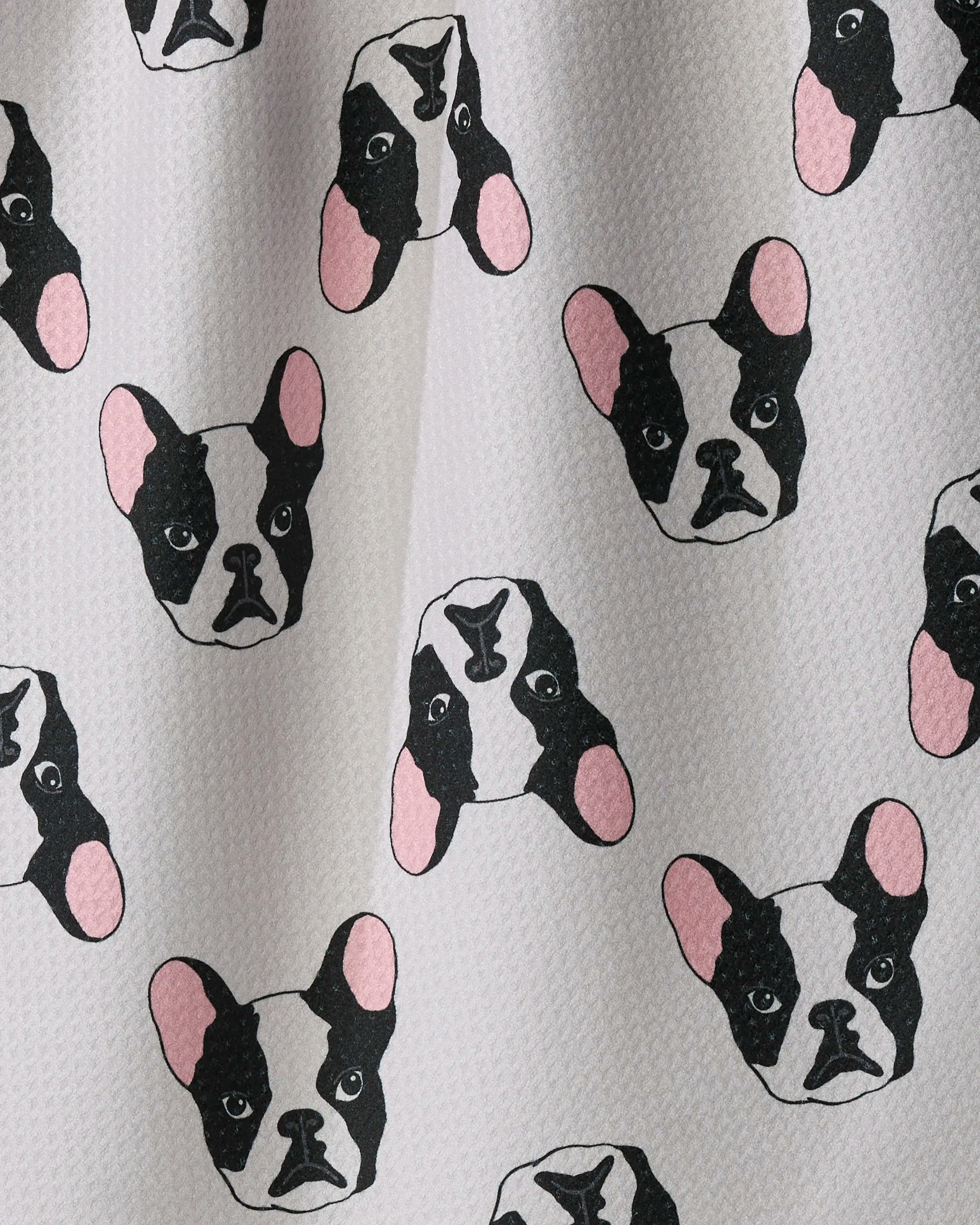 The Geometry Frenchie Faces kitchen tea towel features multiple cartoon black and white dog faces with pink ears on a light textured background. Crafted from recycled materials, this ultra-absorbent towel brings both charm and sustainability to your kitchen décor.