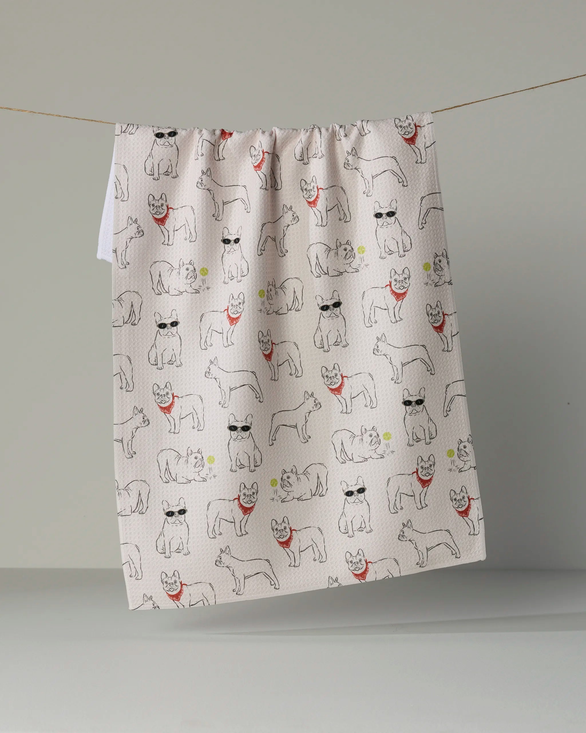 The Geometry “Frenchie Frolic” kitchen towel features a playful pattern of cats and dogs sporting sunglasses and red scarves, set against a beige background.