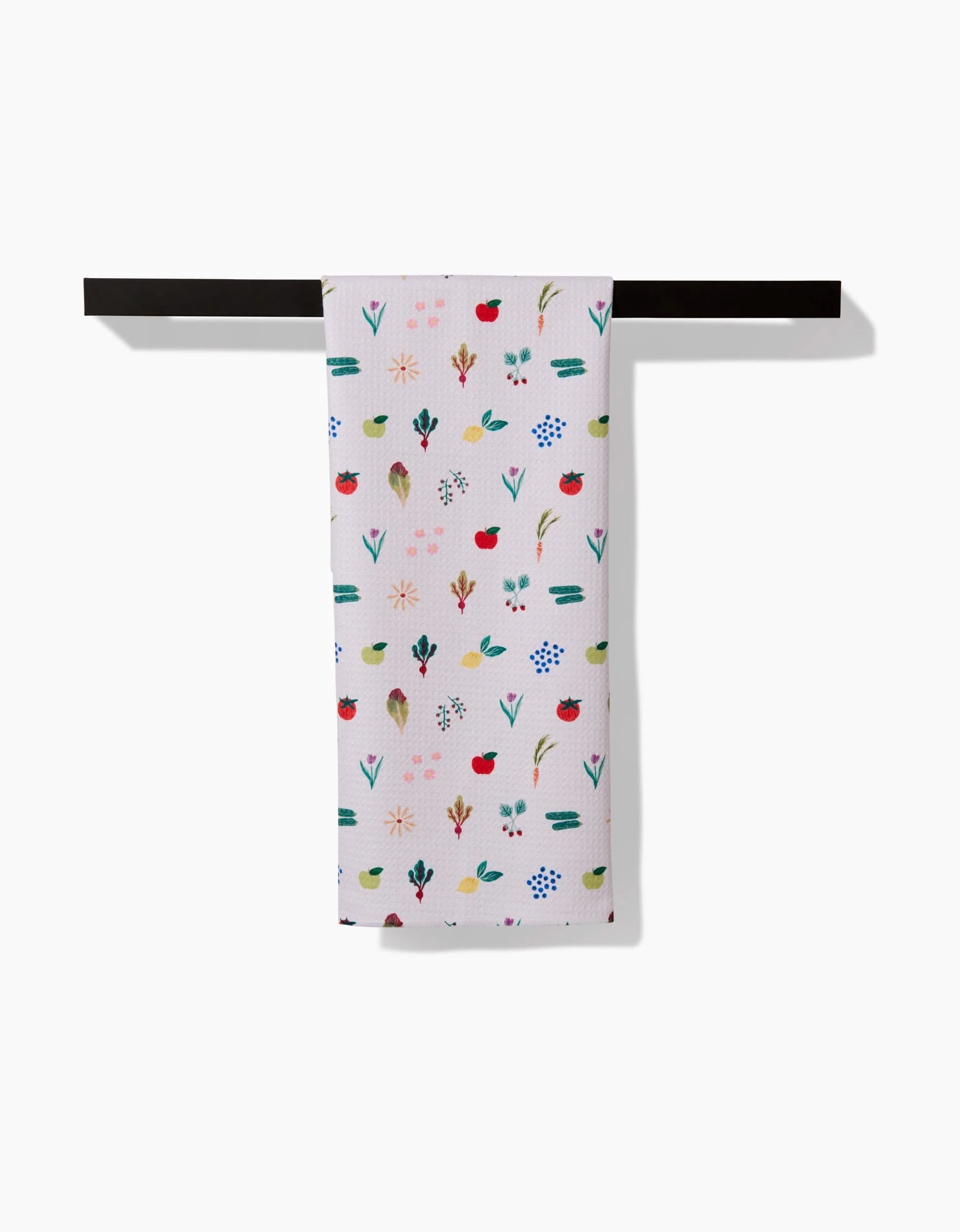 A Brittany Jepsen Fresh Produce tea towel featuring a colorful floral and plant design hangs neatly on a horizontal black bar against a white background.