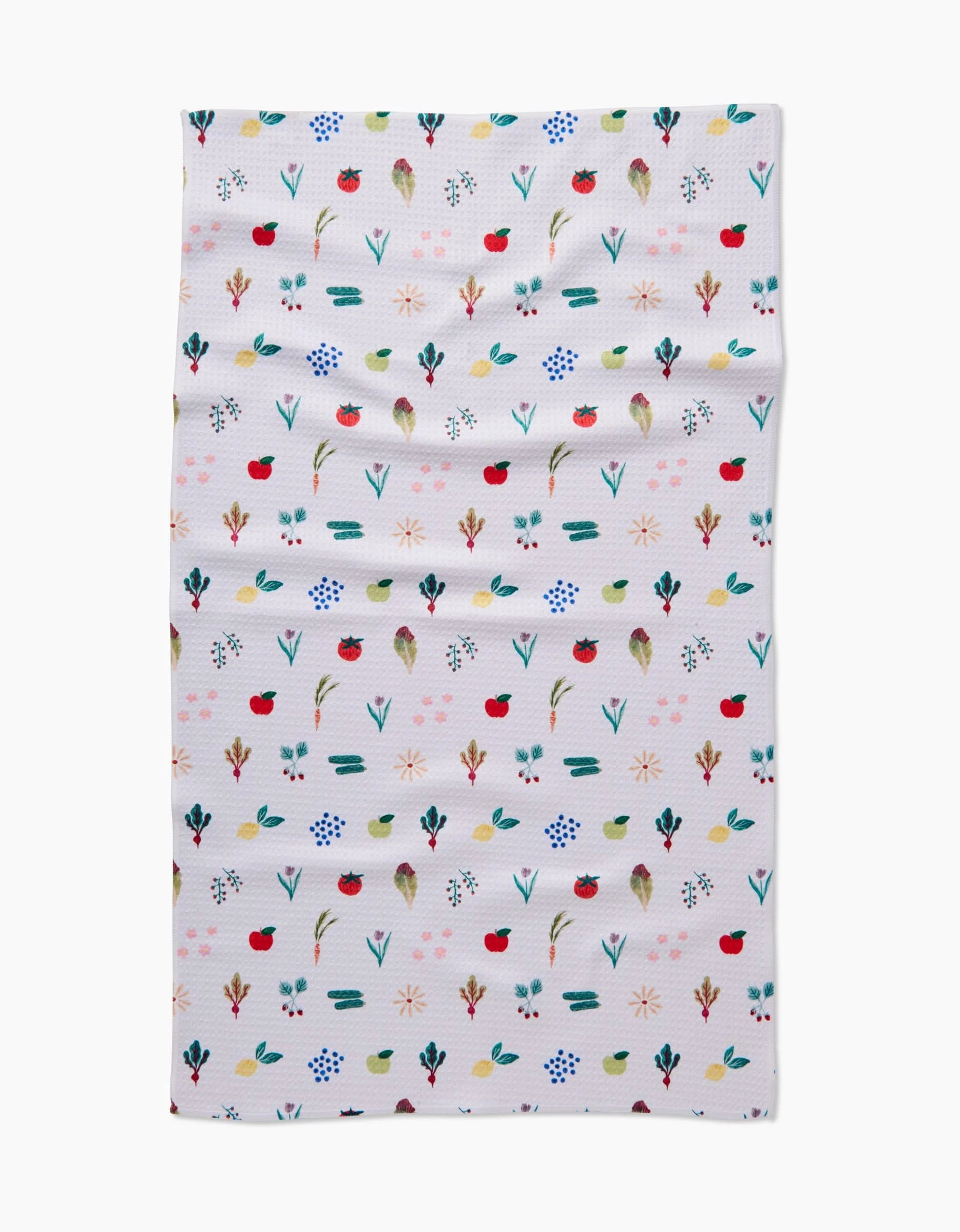 The Brittany Jepsen Fresh Produce tea towel features small, colorful red, blue, green, and yellow flowers and leaves arranged in neat rows on white fabric with a slightly wrinkled texture.