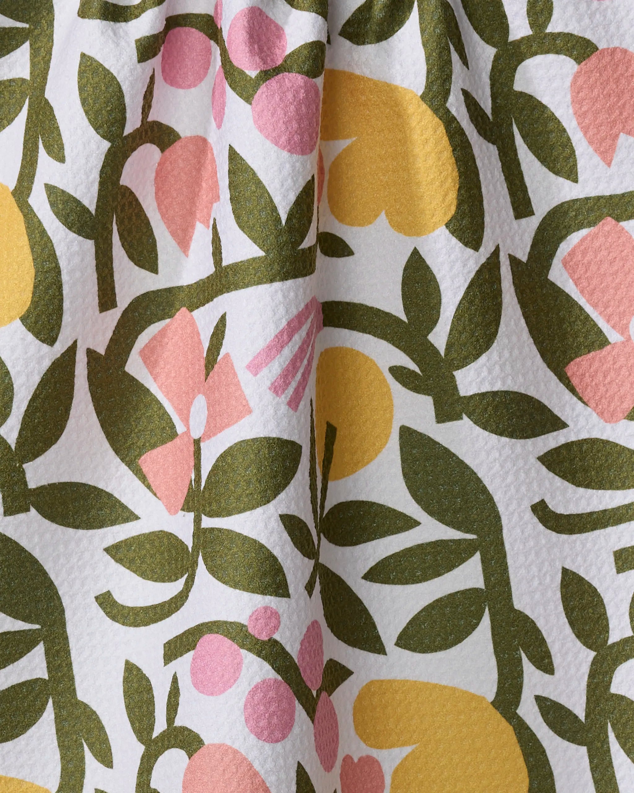 A close-up of Lisa Nelson's Fresh Vines tea towel shows textured Geoweave fabric made from recycled materials, featuring a colorful floral pattern with green leaves, yellow shapes, and pink flowers on a white background.