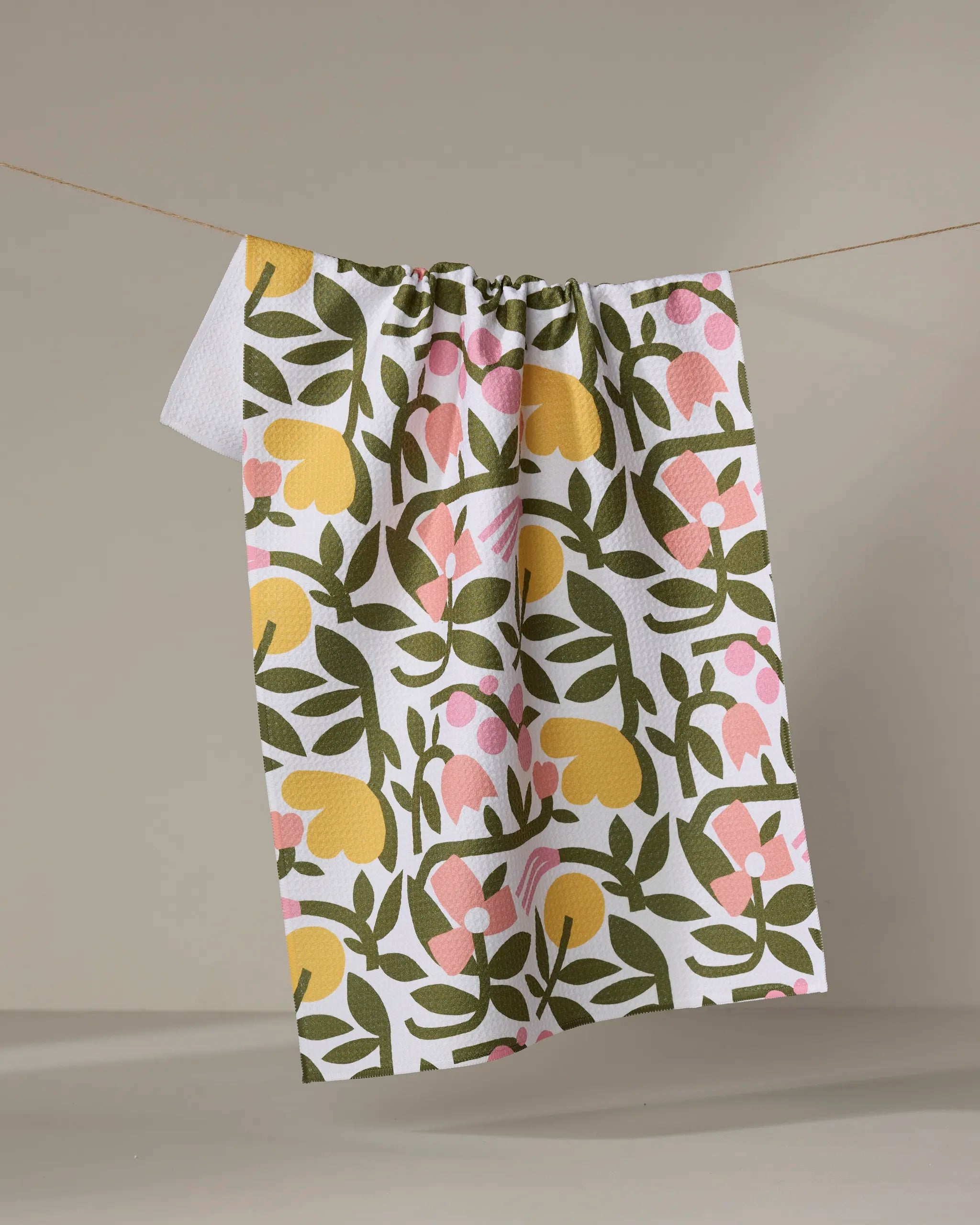 The Fresh Vines tea towel by Lisa Nelson features a colorful green, yellow, and pink floral pattern on white Geoweave fabric. It hangs on a beige string against a neutral background, perfect for everyday use.