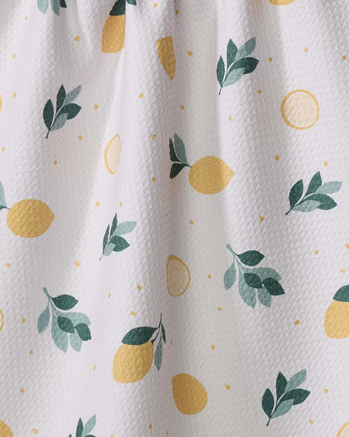 The Sara Mari "Freshly Picked" tea towel features a white textured fabric with yellow lemons, lemon slices, small yellow dots, and green branches. Made from quick-drying recycled materials for everyday convenience.
