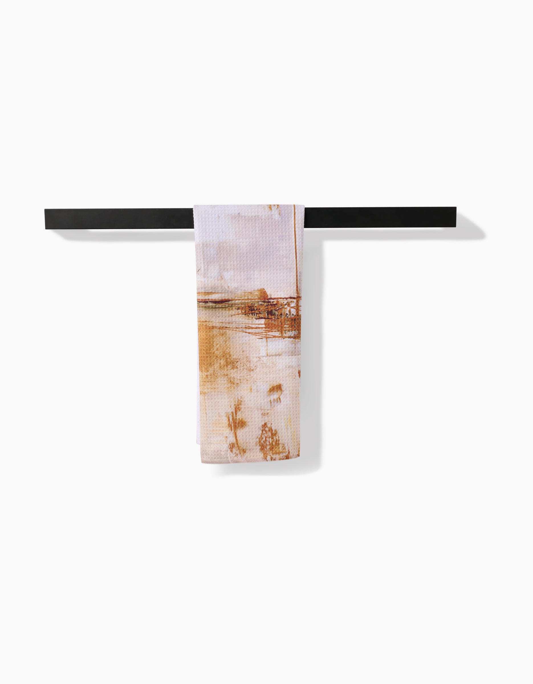 The Friction tea towel by Jennifer Janesko, featuring a brown and beige scenic print, hangs on a black rack against a white background. Crafted from soft Geoweave™ fabric, it offers superior absorbency.