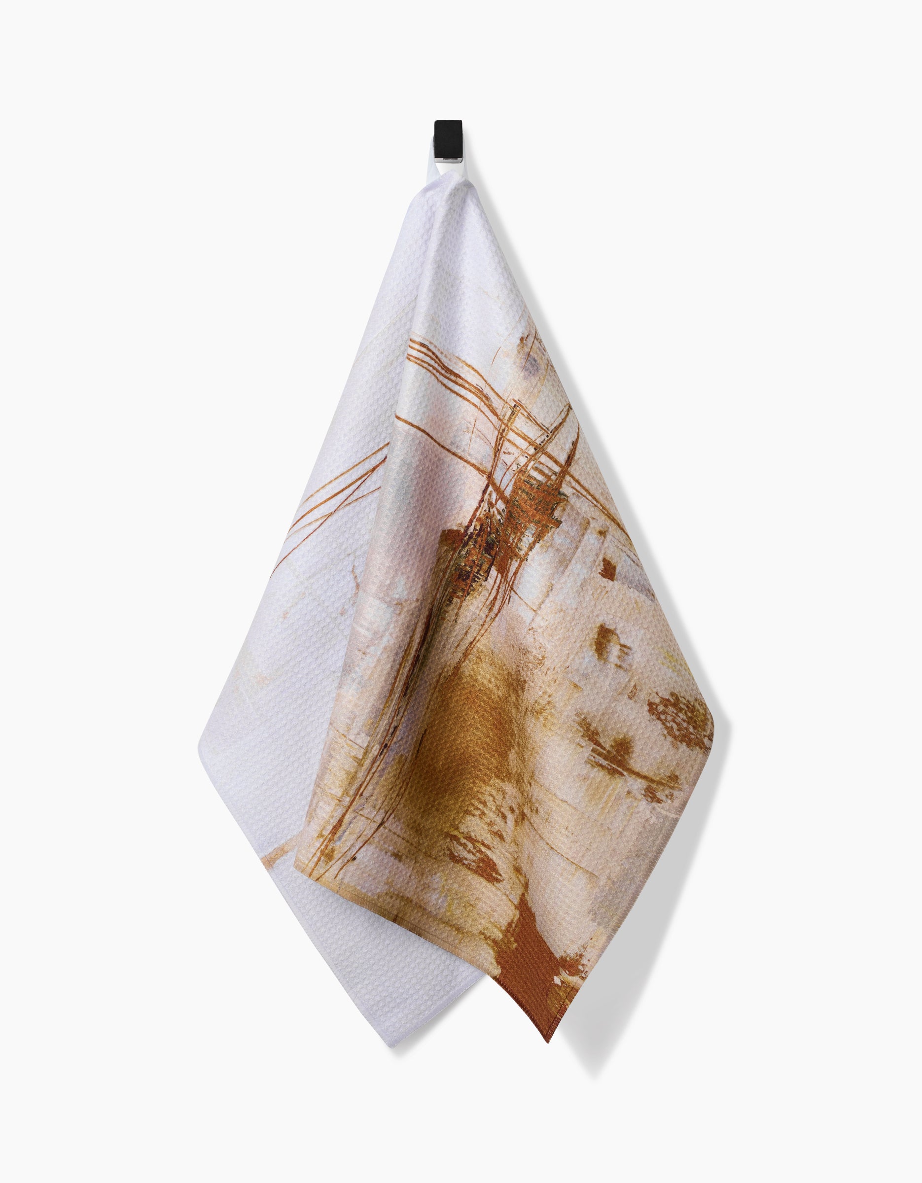 The Friction tea towel by Jennifer Janesko, made from recycled materials and featuring an abstract brown and tan linear design, hangs from a black hook against a plain white background.