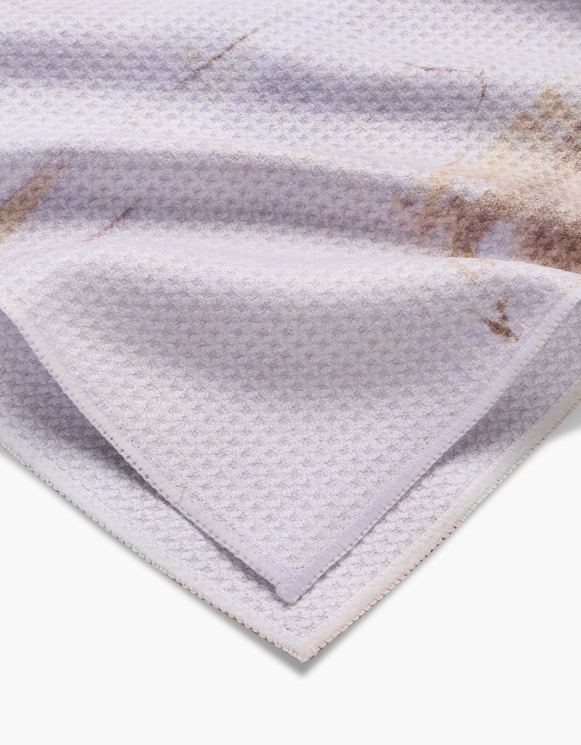A close-up of the Friction tea towel by Jennifer Janesko, in light purple Geoweave™ fabric with a subtle pattern, a folded corner, and faint brownish stains.