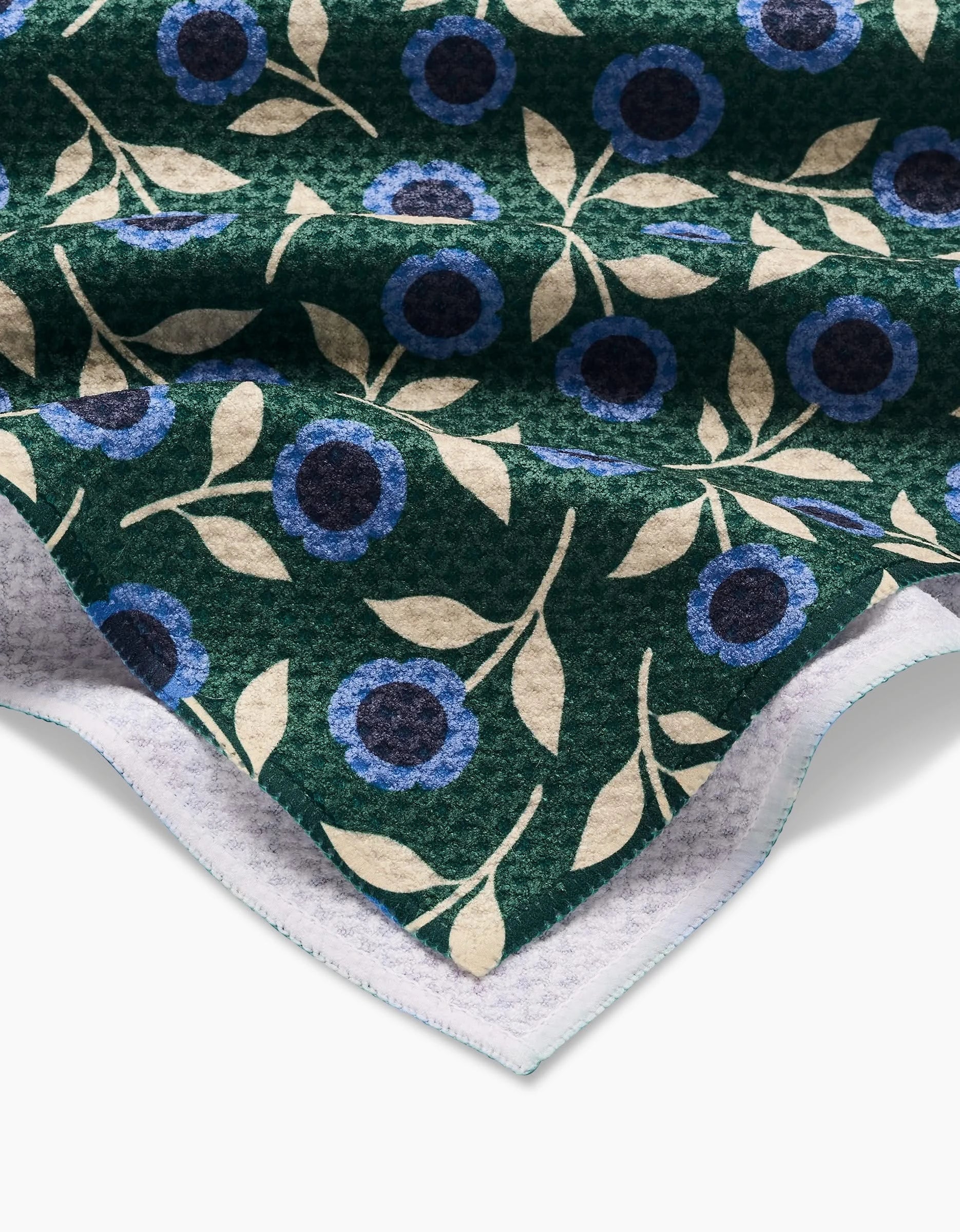 A close-up of Megan Kampa’s Friendly Floral Blue green tea towel shows blue and cream flowers with beige leaves, the textured Geoweave fabric surface, and white underside—all crafted from recycled materials.