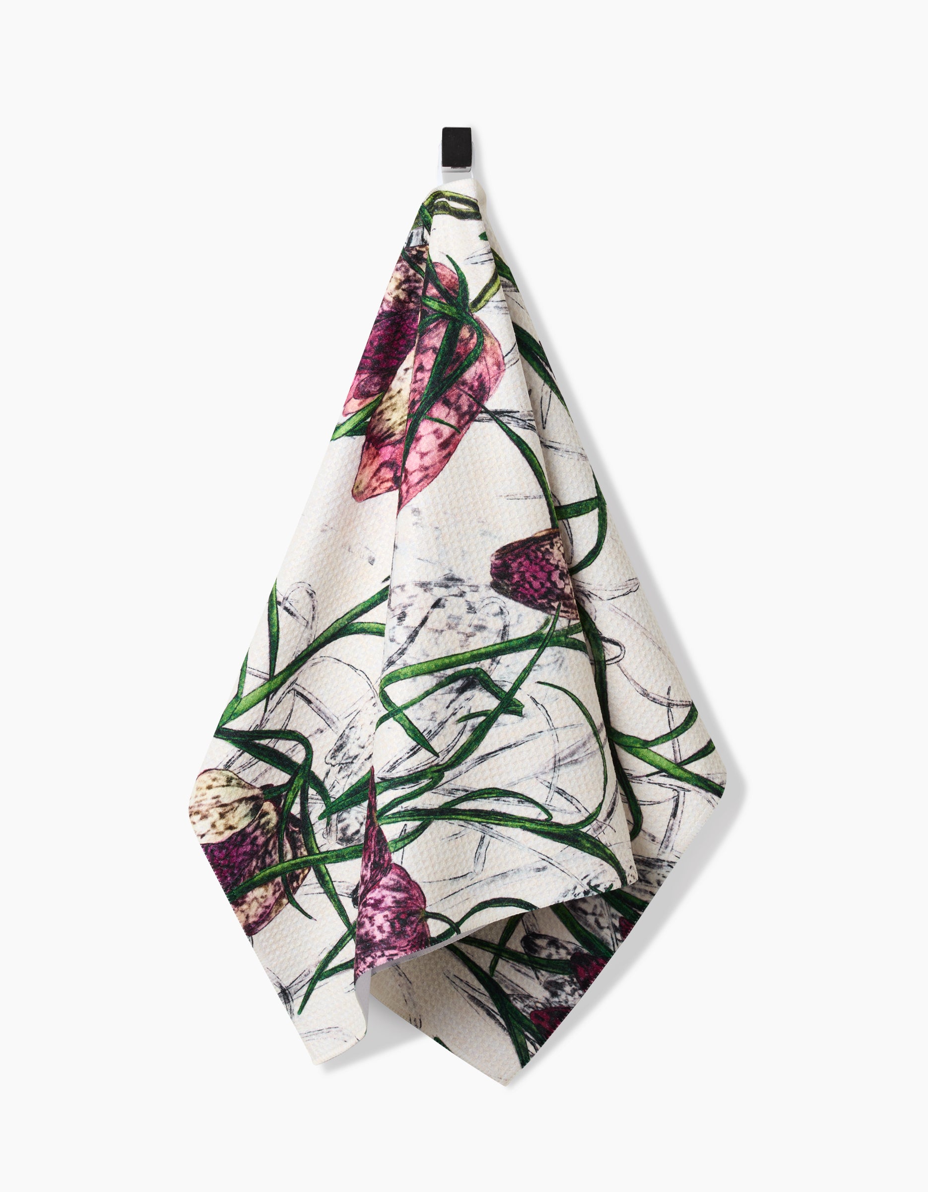 The Fritillaria kitchen towel by Pascale Dilger, crafted from recycled materials and featuring a purple and green botanical print, hangs from a black hook against a plain white background.
