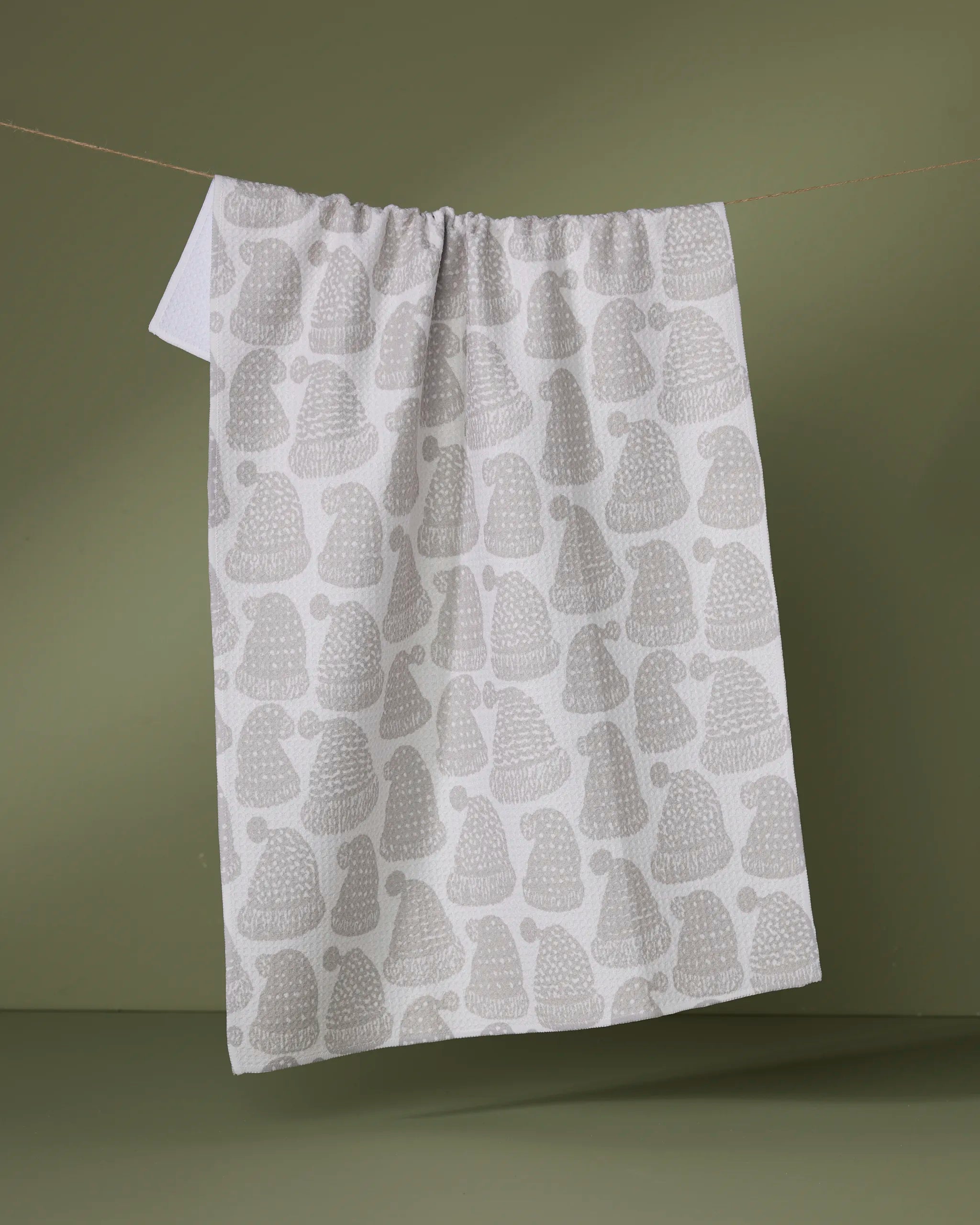 The Geometry Frostcap kitchen tea towel, featuring a pattern of light gray hedgehogs on white and made from recycled materials, hangs on a clothesline against a plain olive green background.