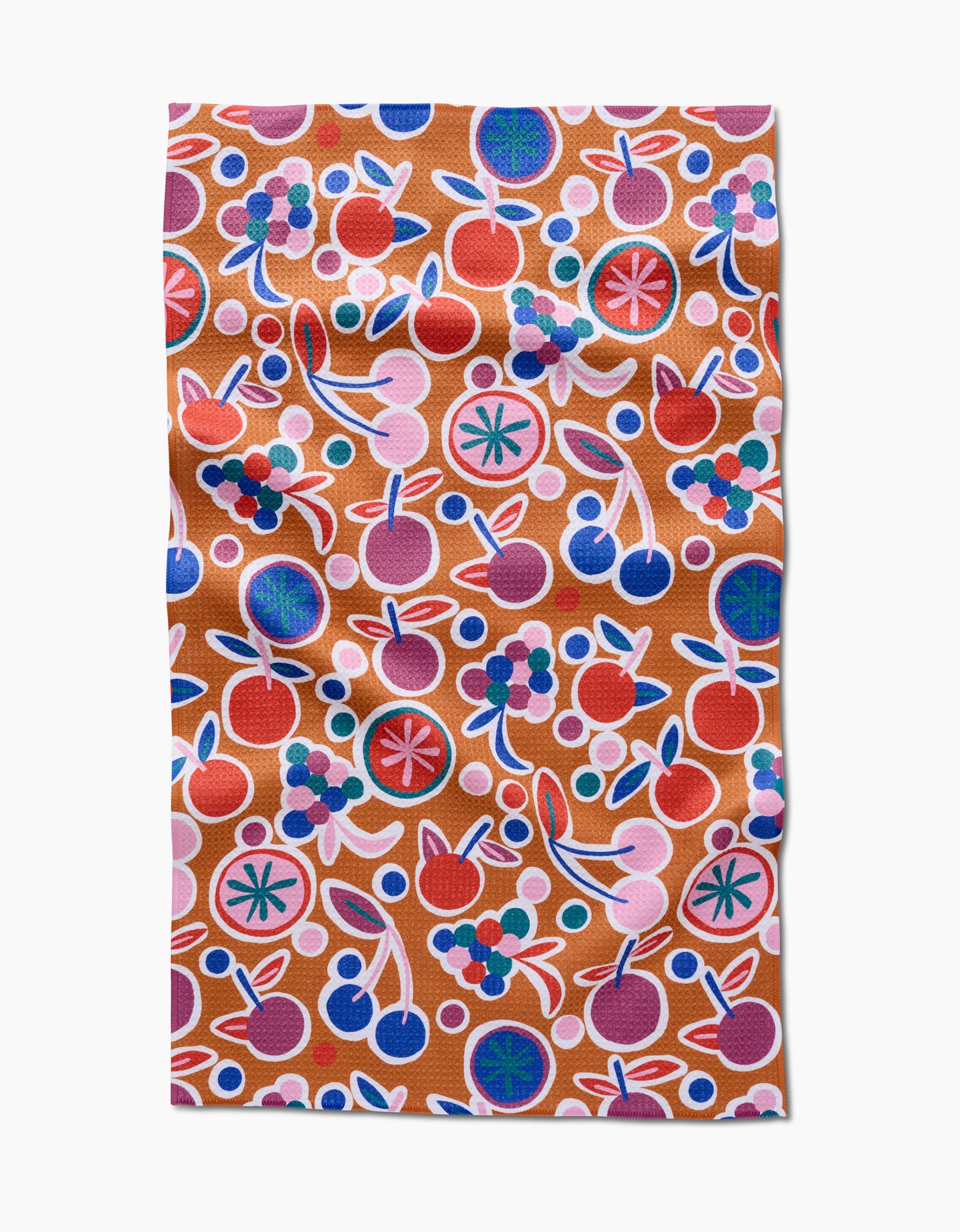 The Fruits Party tea towel by Claire Iglesias features a colorful cherry, berry, and leaf design in red, blue, green, purple, and pink on light brown ultra-absorbent fabric with a slightly wrinkled texture.
