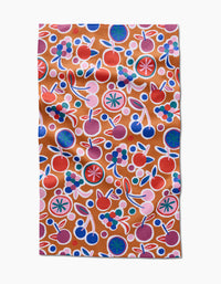 The Fruits Party tea towel by Claire Iglesias features a colorful cherry, berry, and leaf design in red, blue, green, purple, and pink on light brown ultra-absorbent fabric with a slightly wrinkled texture.