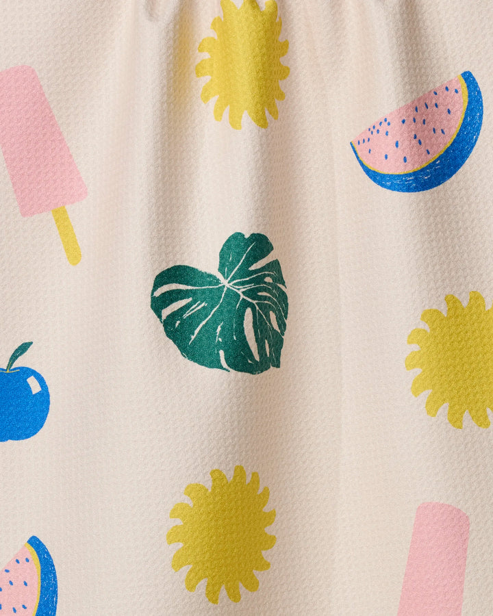 The Fruity Pop tea towel by Geometry features playful patterns of a green monstera leaf, yellow suns, blue apples, pink popsicles, and pink watermelons with blue rind on a light textured background.