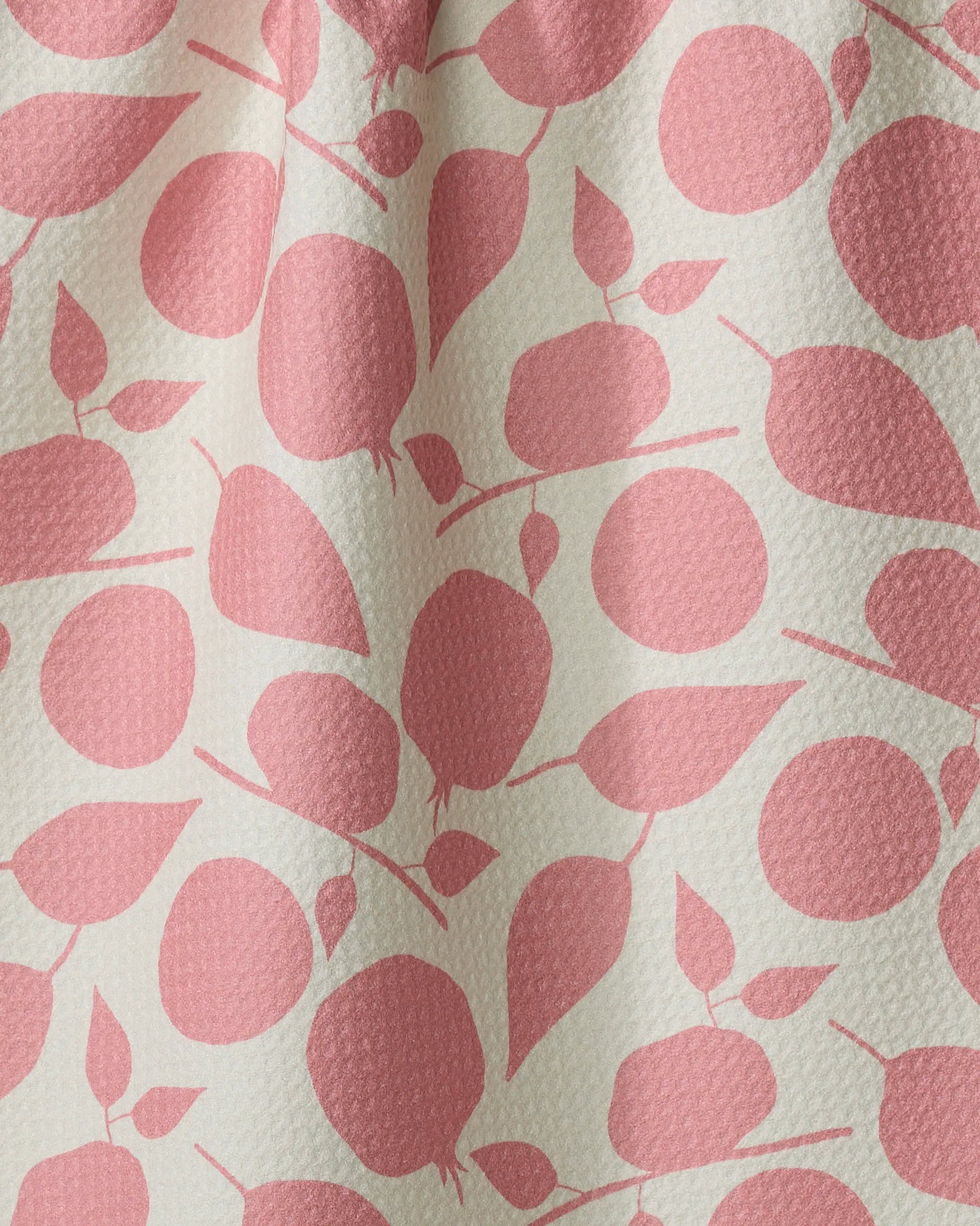 The Fruity Toss tea towel by Lizzie Clark features a white background with a repeating pattern of pink, stylized fruit and leaves. Made from recycled materials, its textured fabric displays subtle folds and shadows.