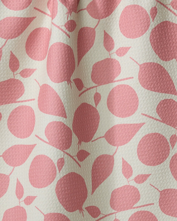 The Fruity Toss tea towel by Lizzie Clark features a white background with a repeating pattern of pink, stylized fruit and leaves. Made from recycled materials, its textured fabric displays subtle folds and shadows.