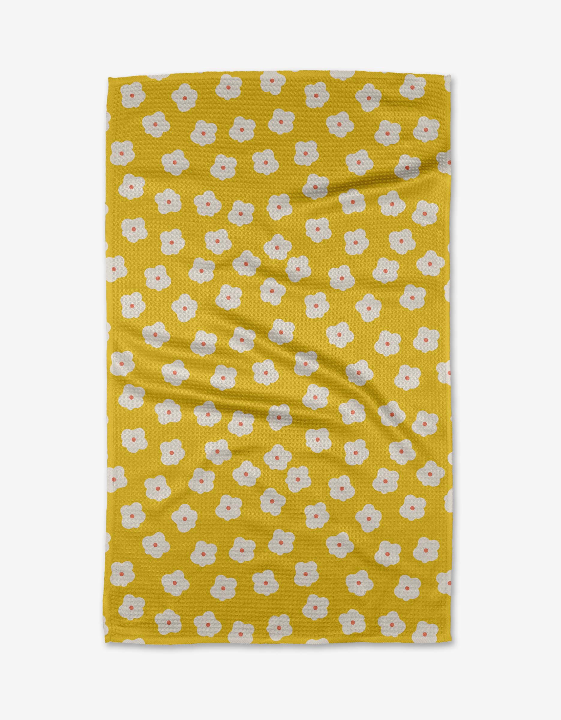 The Sara Mari “Garden Crush” tea towel features a yellow base with scattered small white flowers with orange centers. Laid flat, its gentle folds highlight its eco-friendly recycled material construction.