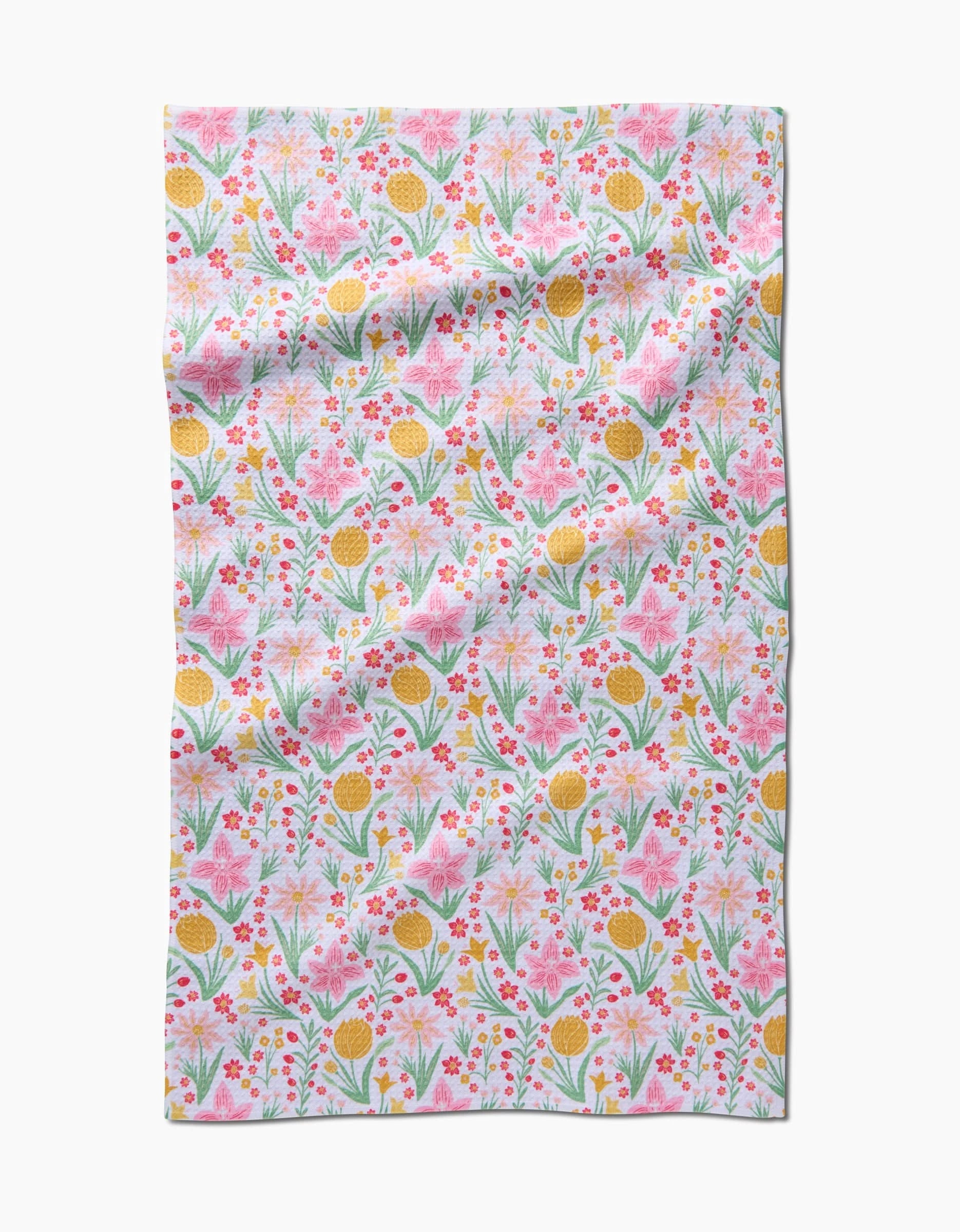 Danelys Sidron’s “Garden of Light” is a rectangular cloth made from recycled materials, featuring pink, yellow, and red flowers with green leaves on a white background. The slightly wrinkled fabric shows off its colorful floral pattern.