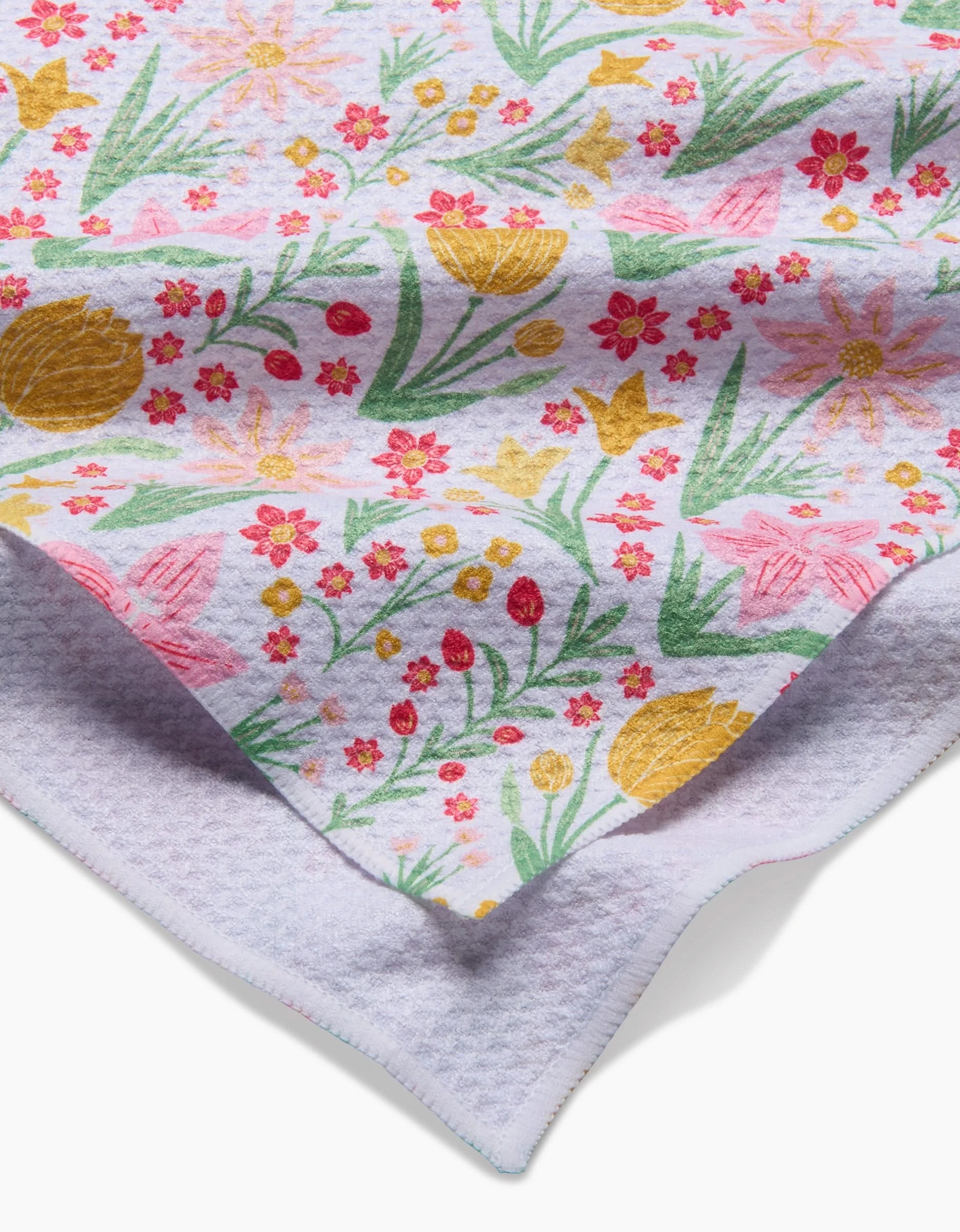 A close-up of the Garden of Light tea towel by Danelys Sidron, made with Geoweave fabric. The towel displays a colorful floral pattern with yellow, pink, and red flowers on white, highlighting its texture and stitched edge.