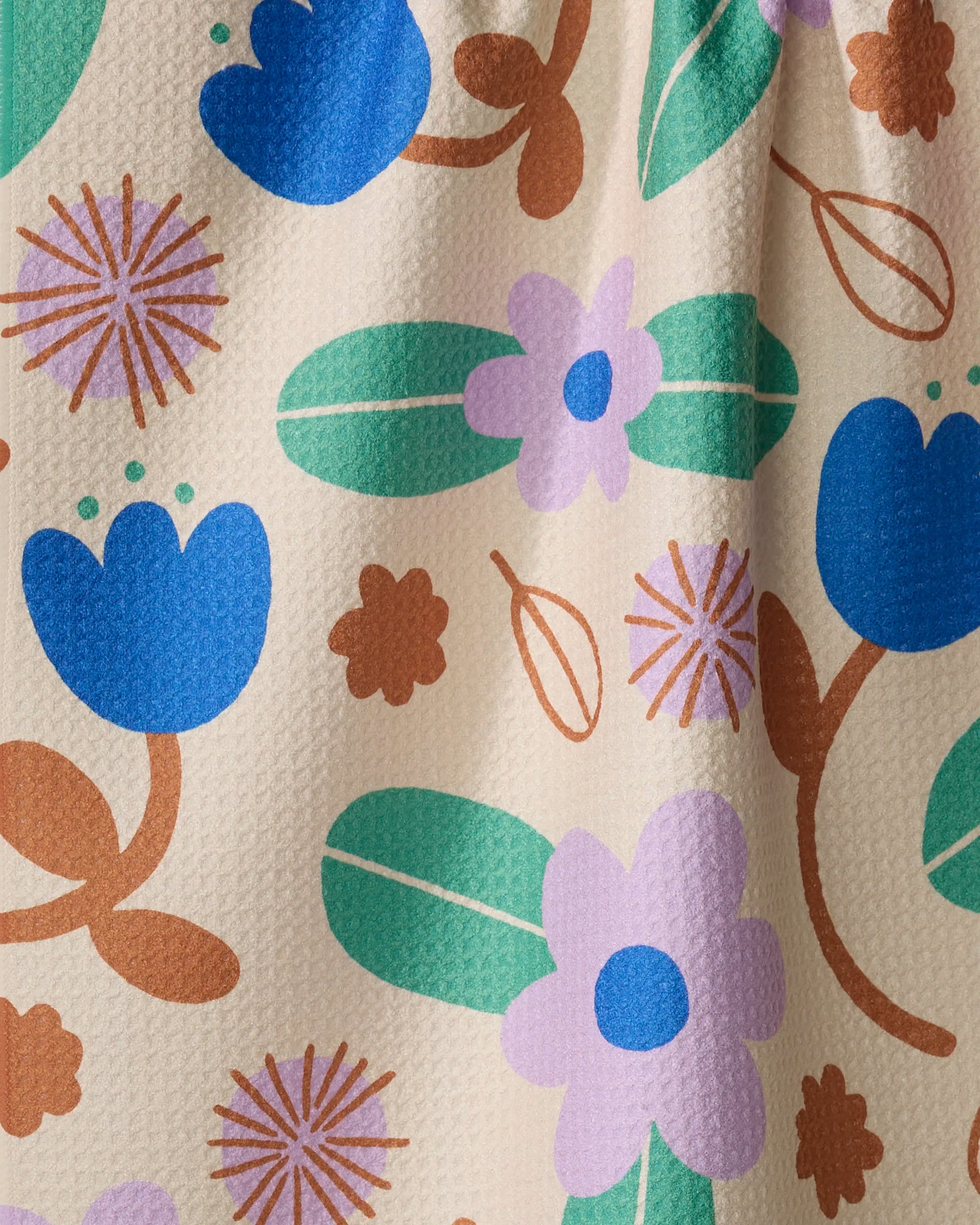A close-up of Beetle Ink Co.'s Garden Patch recycled kitchen towel, featuring a colorful floral pattern with blue, purple, and brown flowers plus green leaves on a textured off-white background.