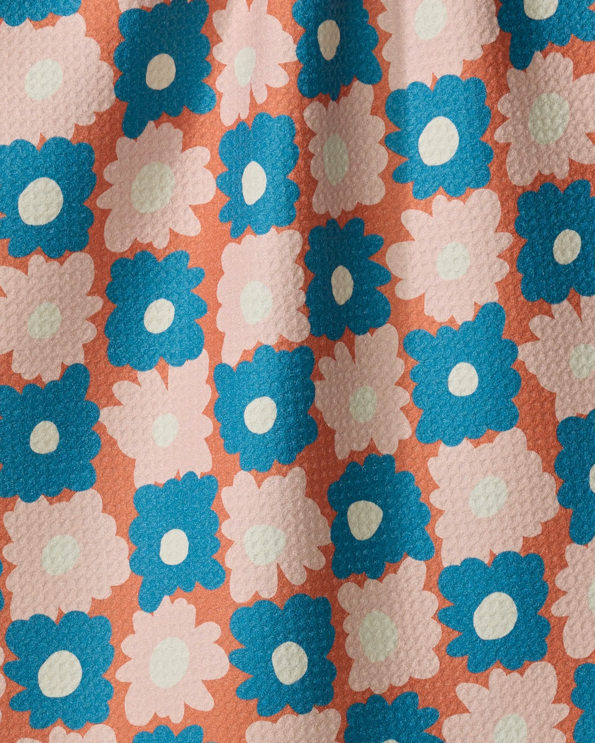 Garden Plot by Kelsey Weigl is a tea towel made from recycled materials, featuring rows of blue and light pink stylized flowers with white centers on a peach background. The textured fabric displays gentle folds and shadows.