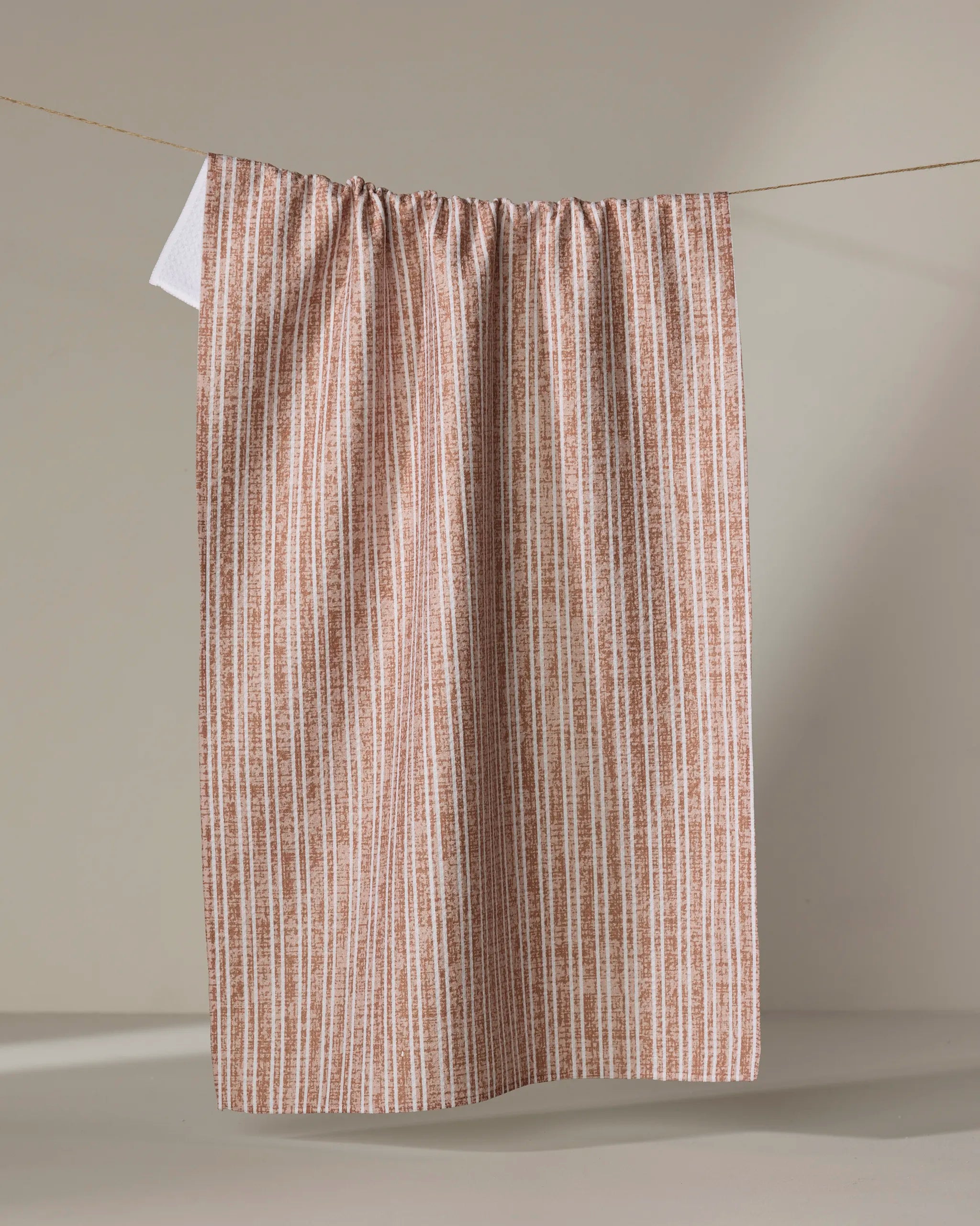 The Becki Owens Garff Rust recycled kitchen towel, featuring brown and white stripes, hangs on a clothesline against a neutral background.