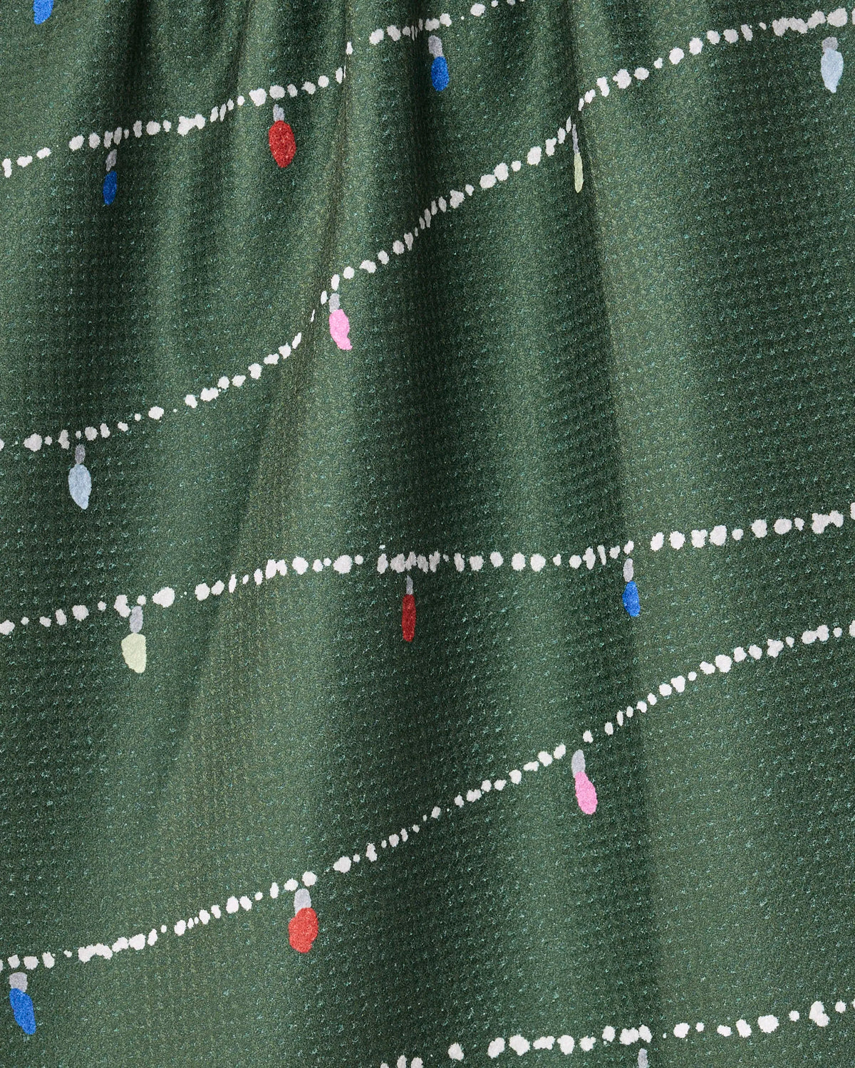 Add festive cheer to your kitchen with the Geometry Garland Glow tea towel—a green fabric towel adorned with white dotted lines and colorful lightbulb shapes in red, blue, pink, and white reminiscent of holiday string lights. Perfect for everyday use, this ultra-absorbent towel combines vibrant style with practicality.