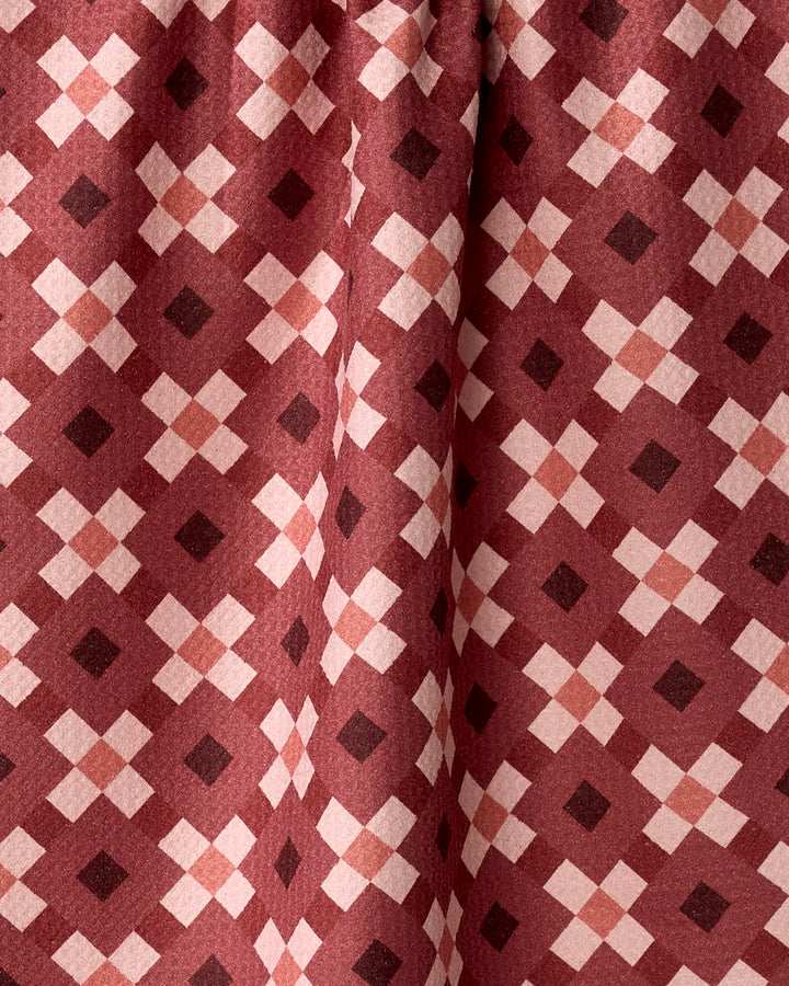 The Garnet Geo by Teri the Butter is a maroon fabric tea towel featuring a symmetrical geometric pattern of light pink and dark red diamonds, made from recycled materials.