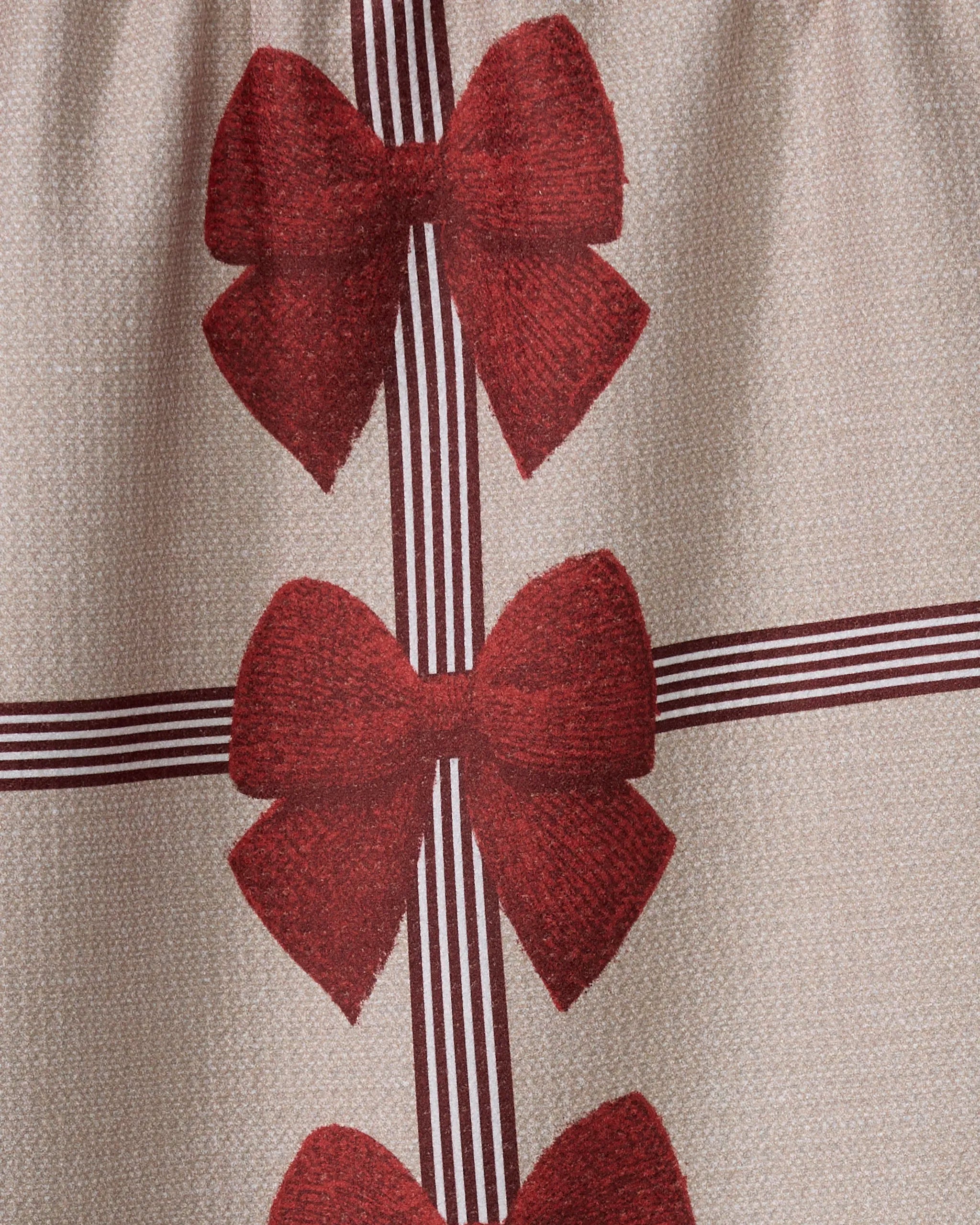 Geometry’s Garnet kitchen towel features a beige base made from recycled materials, adorned with a printed pattern of three large red bows and intersecting dark red stripes for a festive, gift-wrapped look.