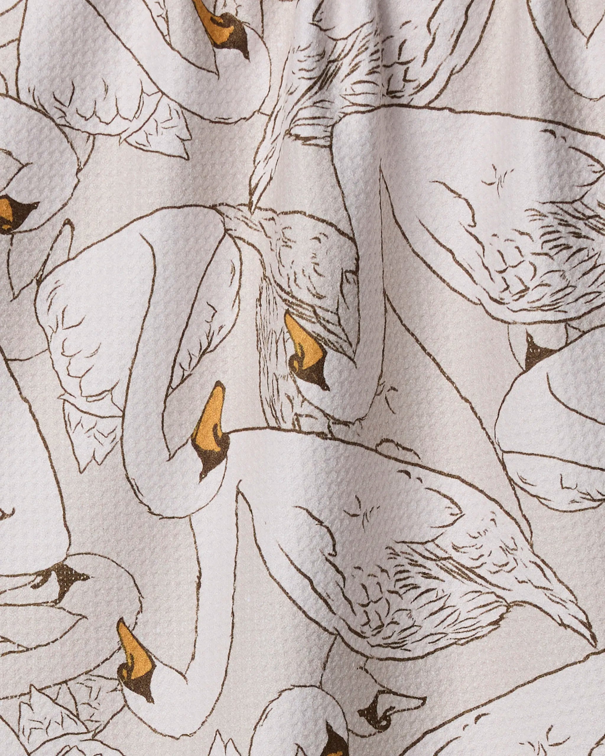 Geometry’s Gentle Strength kitchen towel is made from recycled materials and features illustrated white swans with orange beaks, arranged in overlapping patterns on a textured light background.