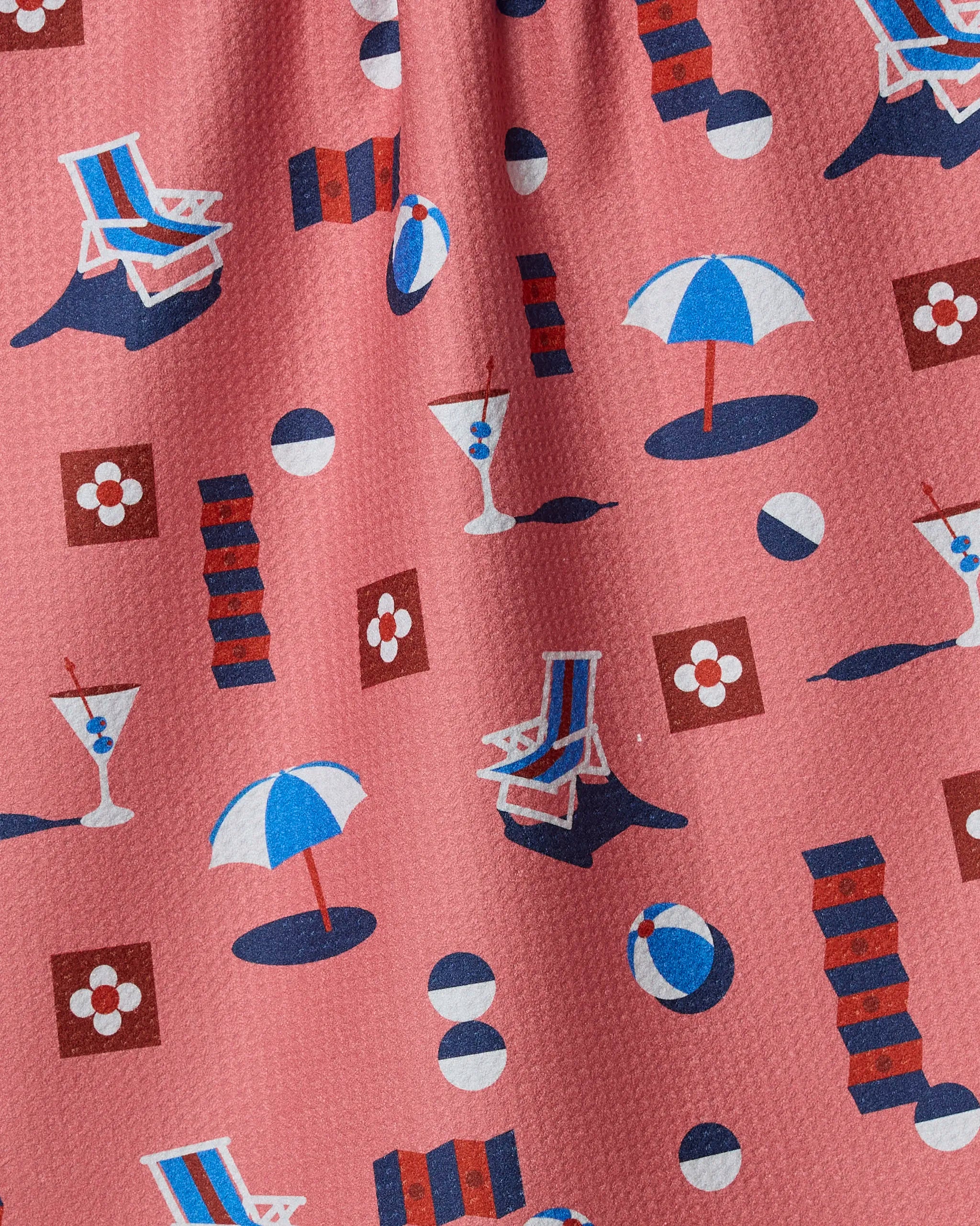 The Geometry Geo Beach Day recycled kitchen towel features a pink pattern with blue, white, and red beach chairs, umbrellas, beach balls, cocktail glasses, and geometric shapes.