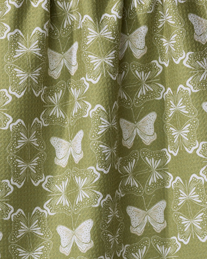 The Geometric Butterflies tea towel by Second Nature Studio features a green fabric with repeating white butterflies in a dotted, symmetrical pattern. Made from quick-drying recycled materials.