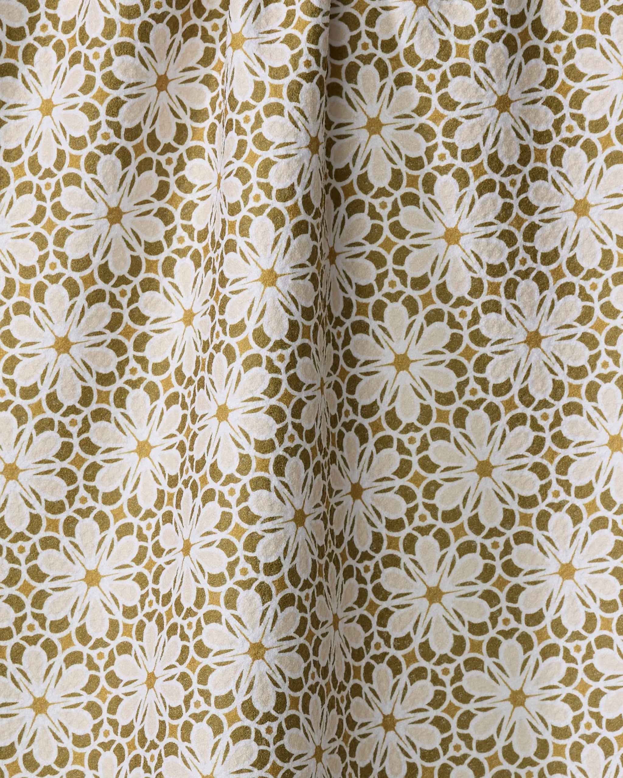 A close-up of the Marta Harvey "Geometric Flower" tea towel, featuring a white and beige floral pattern on olive green, with gentle folds casting soft shadows.