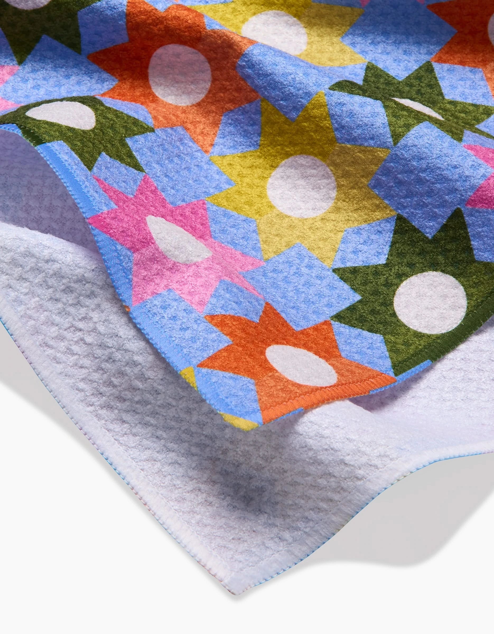 A close-up of Megan Roy’s Geometric Garden shows textured Geoweave fabric with a vibrant geometric star pattern on the front and a soft, light purple recycled back.