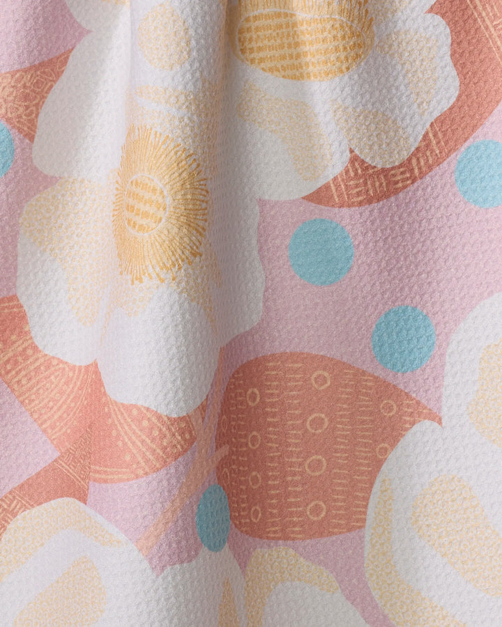 Close-up of the Georgia Rose kitchen towel by Julianne Haness, featuring an eco-friendly, ultra-absorbent textured fabric with large white and yellow flowers, light blue dots, and soft pink shapes on a pastel background.