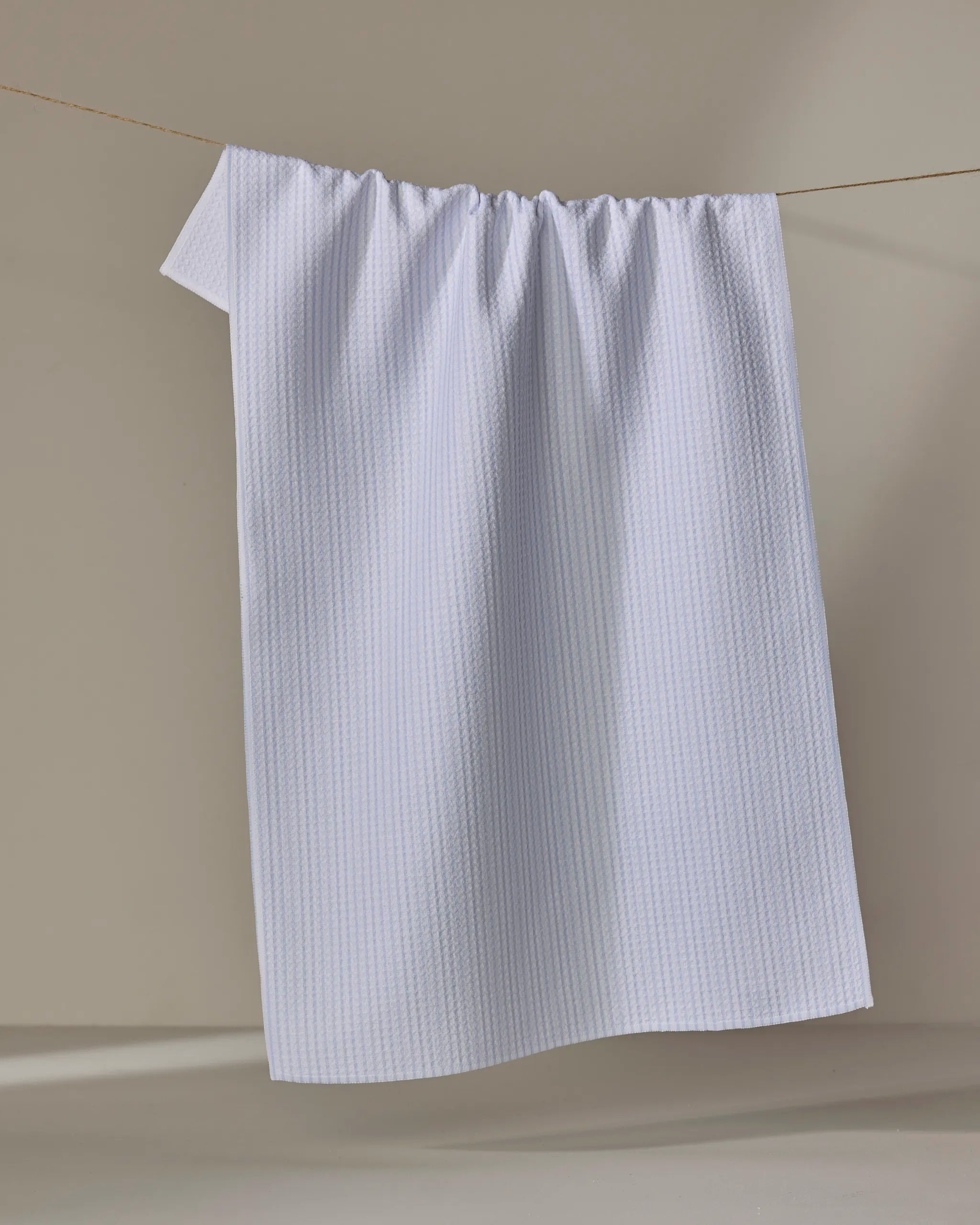 A light blue ultra-absorbent Get In Line towel by The Buy Guide hangs neatly on a thin clothesline against a neutral, softly lit background.