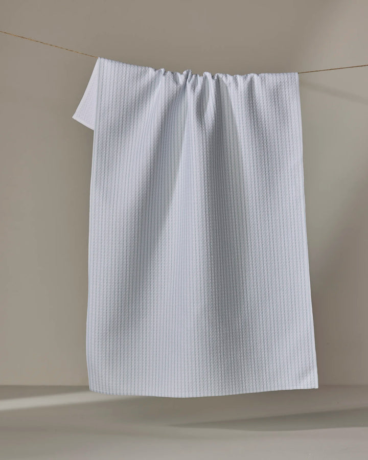 The Buy Guide's Get In Line - Mint tea towel, featuring Geoweave fabric and a textured white design, hangs neatly over a thin clothesline with soft shadows cast on the beige background behind it.