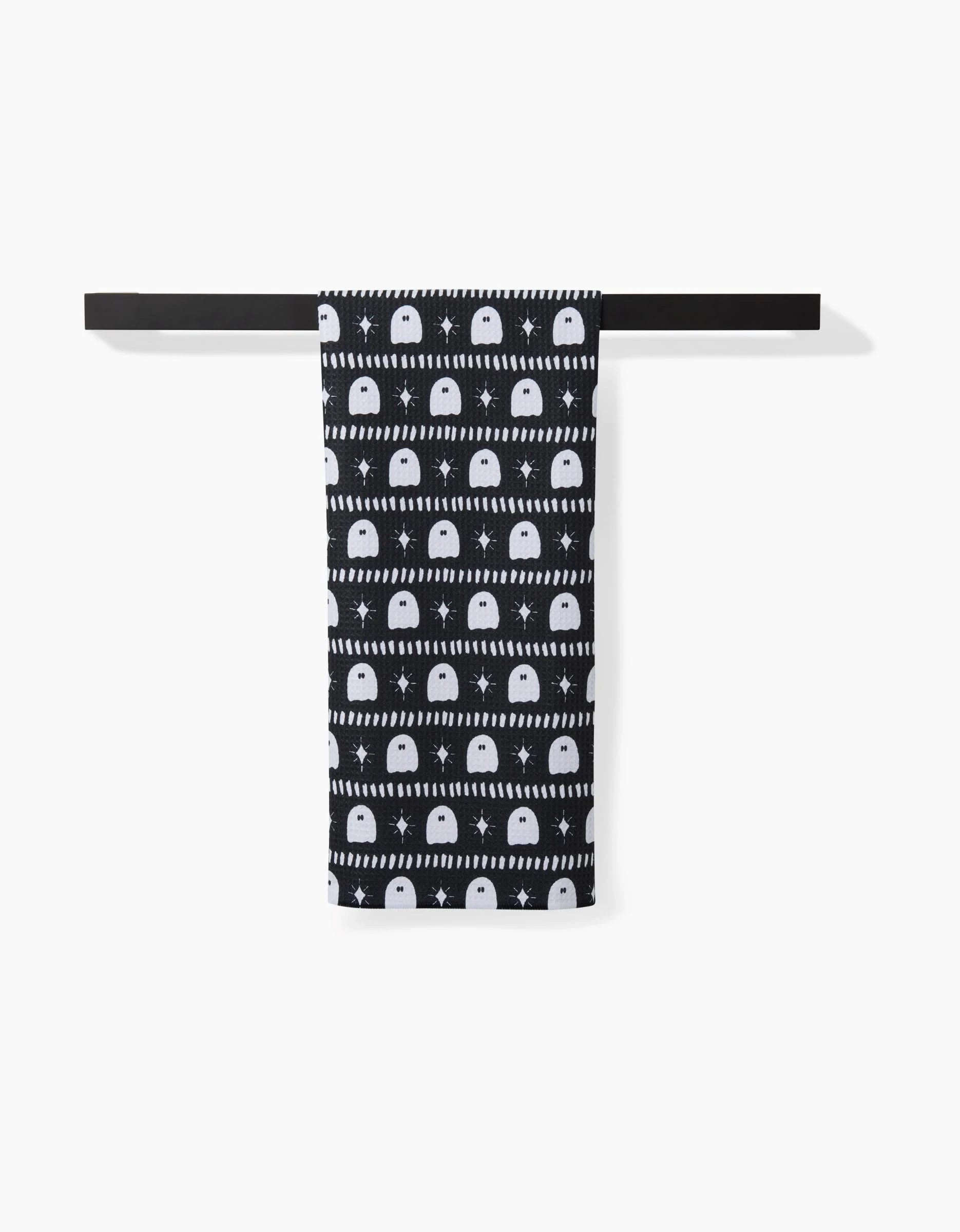 The Ghost Pac Tea Towel by Charlie Rowan Designs features white semicircle patterns on black, crafted from recycled materials, and is shown neatly hanging on a black bar against a white background.