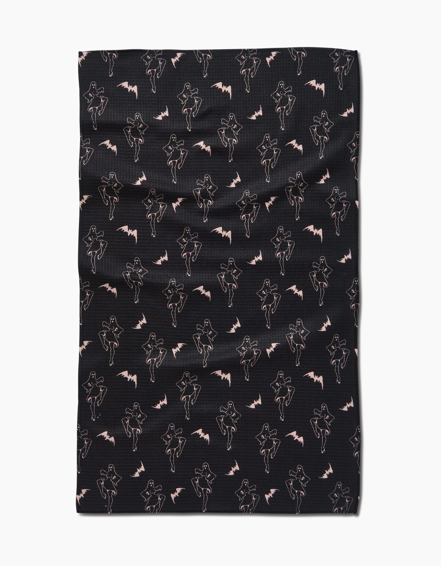 The Ghost Pin Up tea towel by Cole Strem features light pink outlined women with capes and bat motifs on Geoweave fabric, crafted from recycled materials. The black fabric has a slightly wrinkled look.